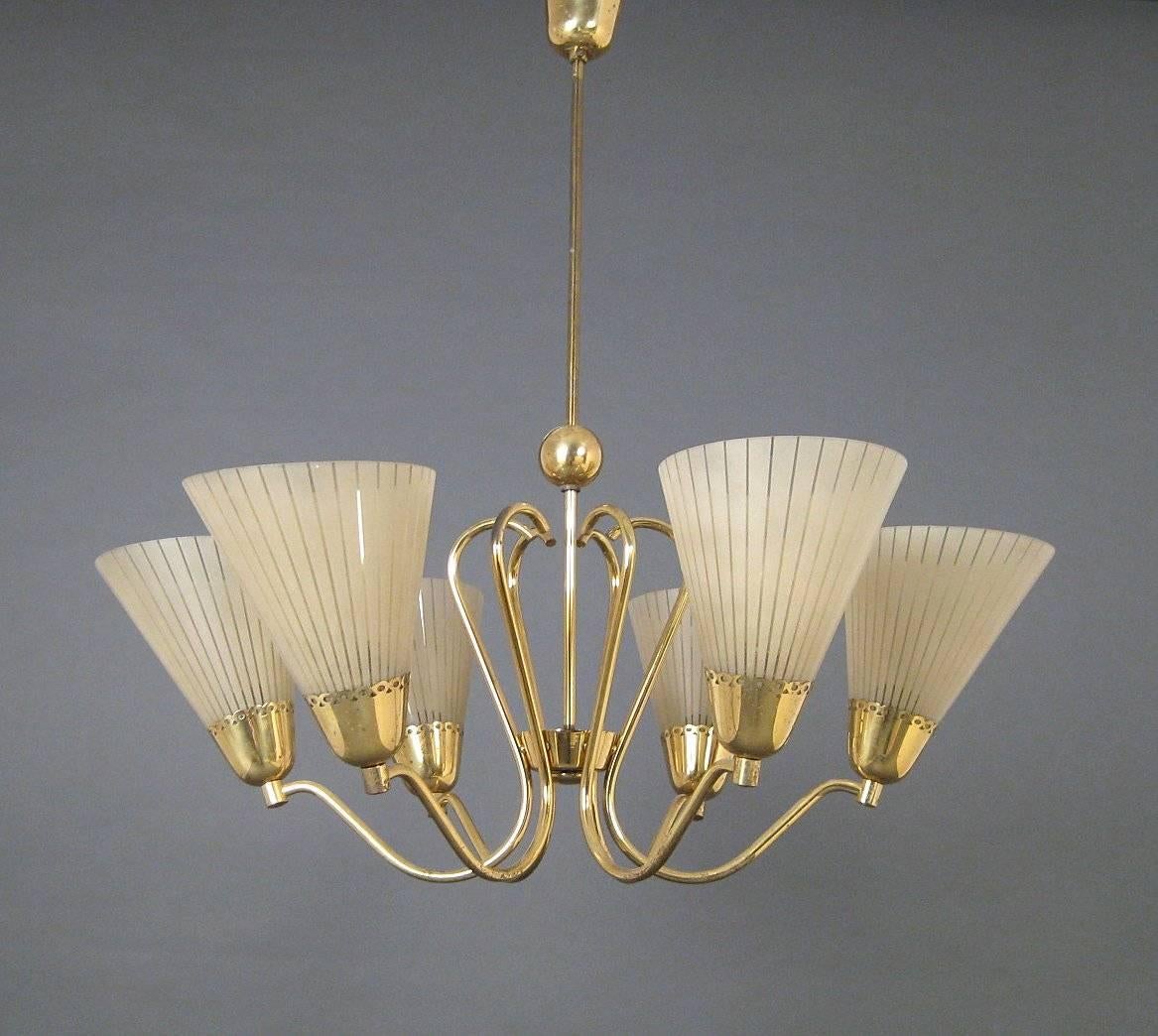 Construction made of brass, fitted with six E14 sockets with cone-shaped diffusers of striped etched glass. Made in Germany in the 1950s.
Measures: Diameter about 80cm, height 80cm.
 