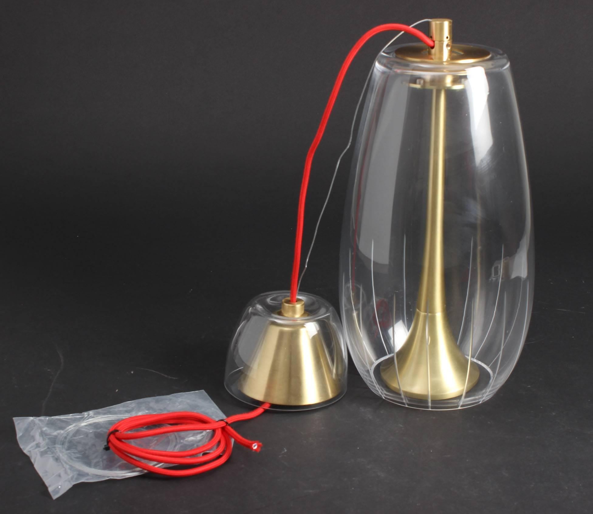 Lampada a sospensione Miles 1C design 2007 di Alfonso Fontal per Modiss.
Miles 1C è un apparecchio a sospensione da soffitto con paralume in cristallo trasparente intagliato e struttura in metallo oro satinato lucido. Include un cavo tessile rosso