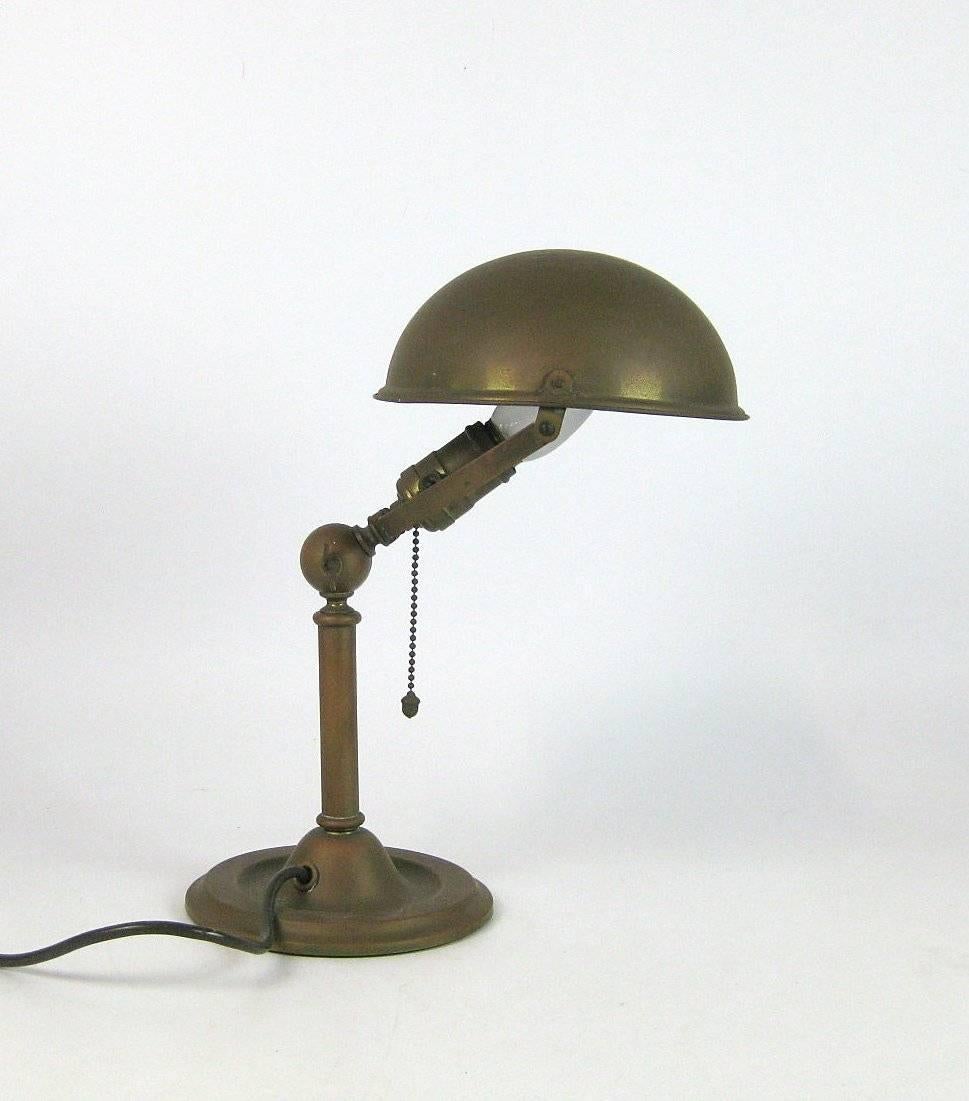 Adjustable table lamp from the 1920s. Construction made of brass sheet, tiltable in articulation, reflector rotatable, fitted with one E 27 socket and pull switch. 
Measure: D. 18.5 cm, H. 38 cm. 
Very good and original condition.