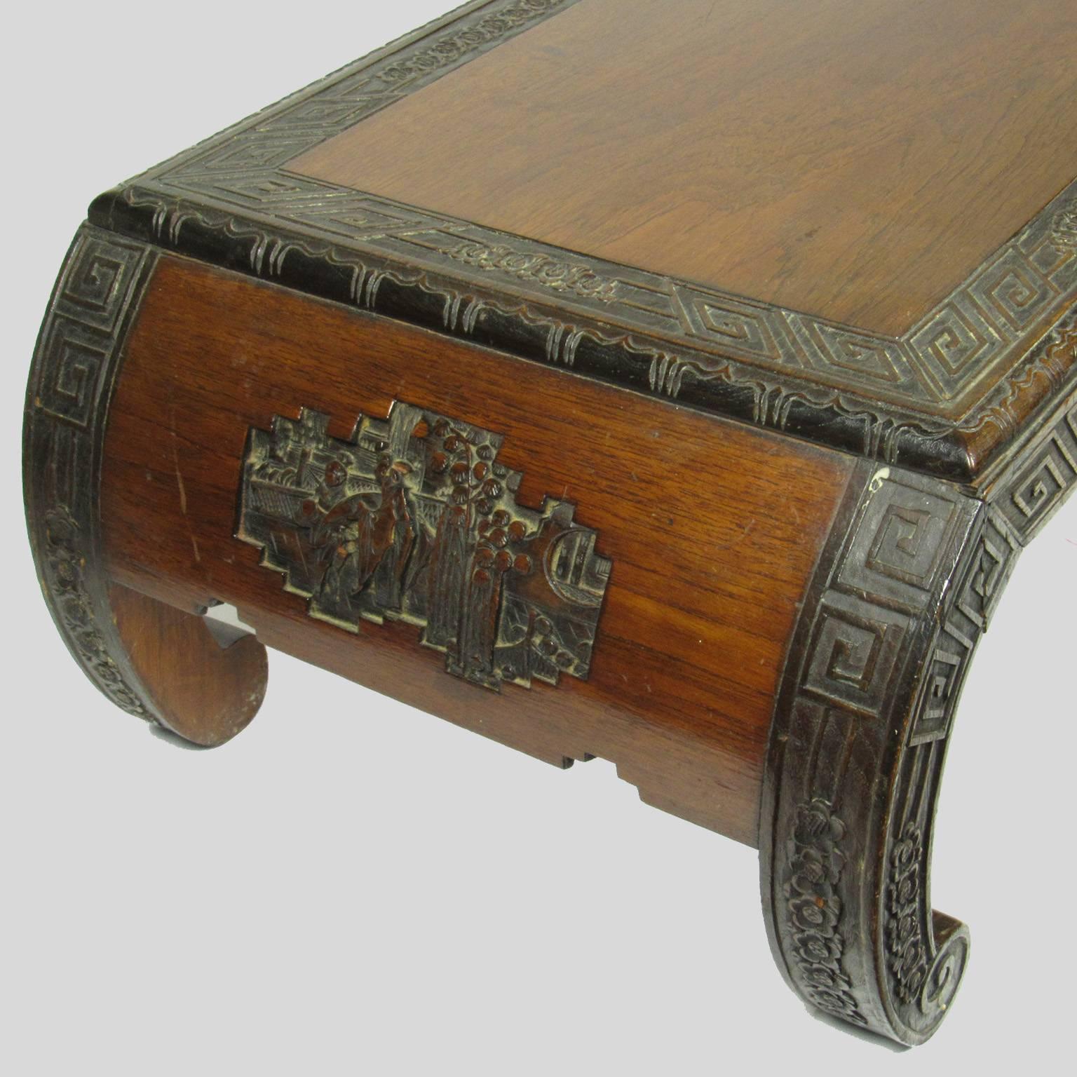 Chinese carved hardwood low table with prunus decoration, two carved figural cartouche, one on each end and scroll feet. Dimensions: 10 5/8 x 36 x 16 in.