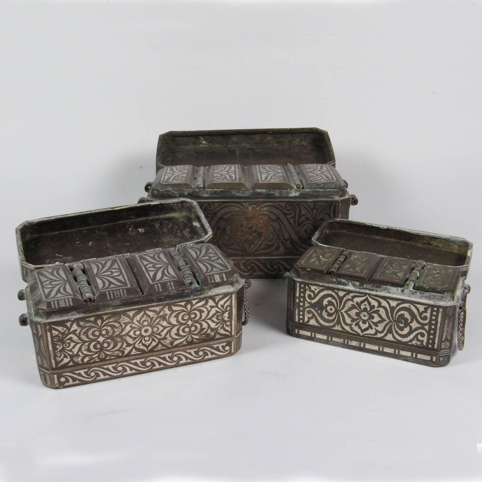 Three antique graduated silver and bronze inlaid betel nut boxes, circa 1900, Philippines. Each bronze box inlaid with silver in the Okir scroll pattern, interior of fitted with central compartment flanked by two smaller compartments for storing