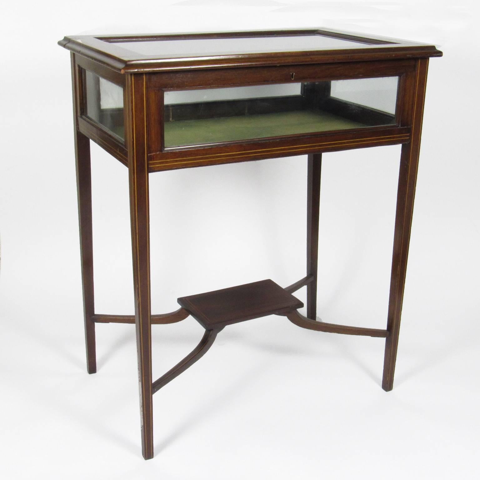 Early to mid-20th century inlaid mahogany vitrine table of rectangular form with glass lift top and green felted interior with lower shelf, raised on string inlaid tapered legs. Measures: Height 29 in., width 24 in., depth 16 in.