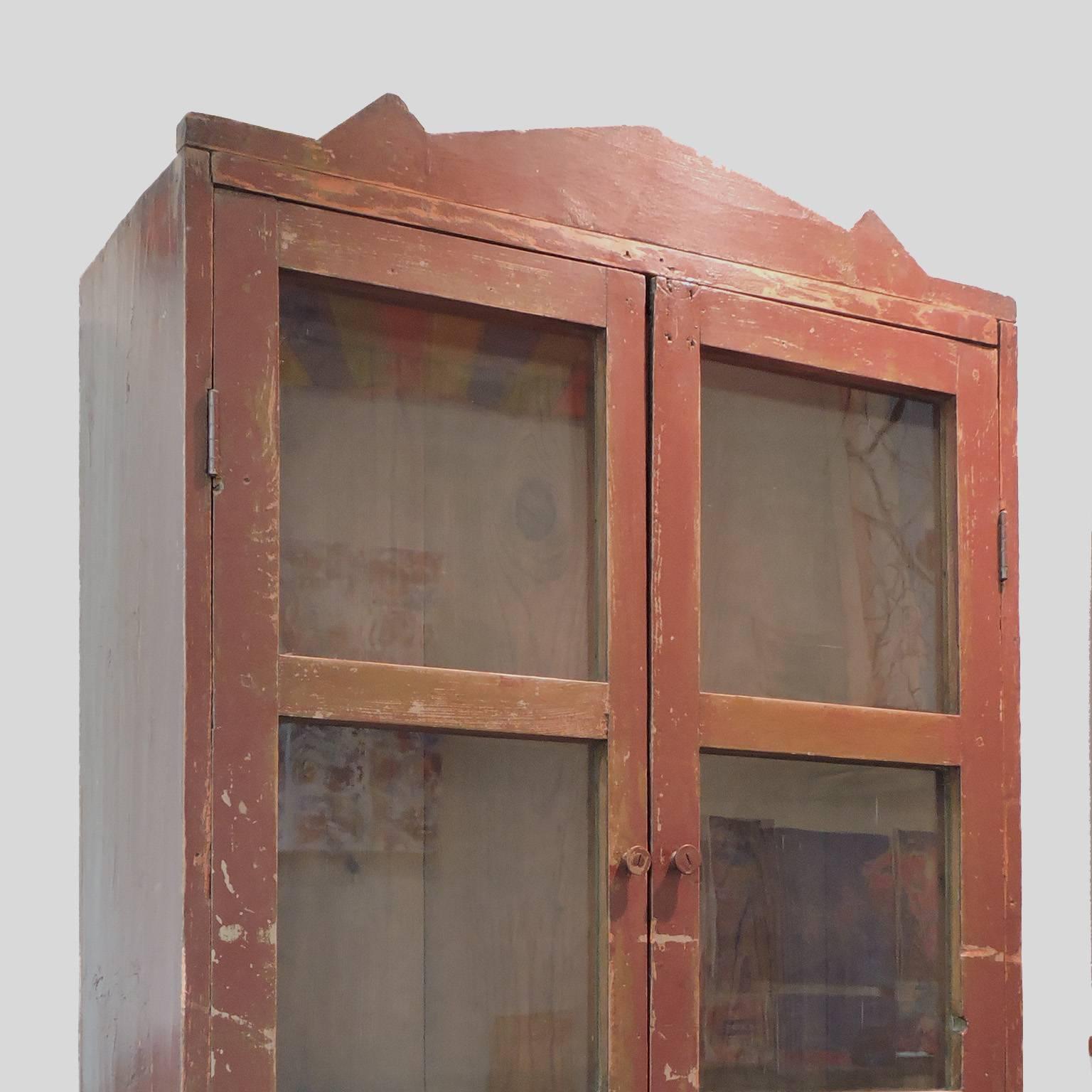 Terrific 19th century Mexican cupboard with original red paint, 19th century. Constructed in one piece with glass doors revealing two shelfs over a cabinet base raised on feet. Dimensions: 80 x 31 1/2 x 22 inches.