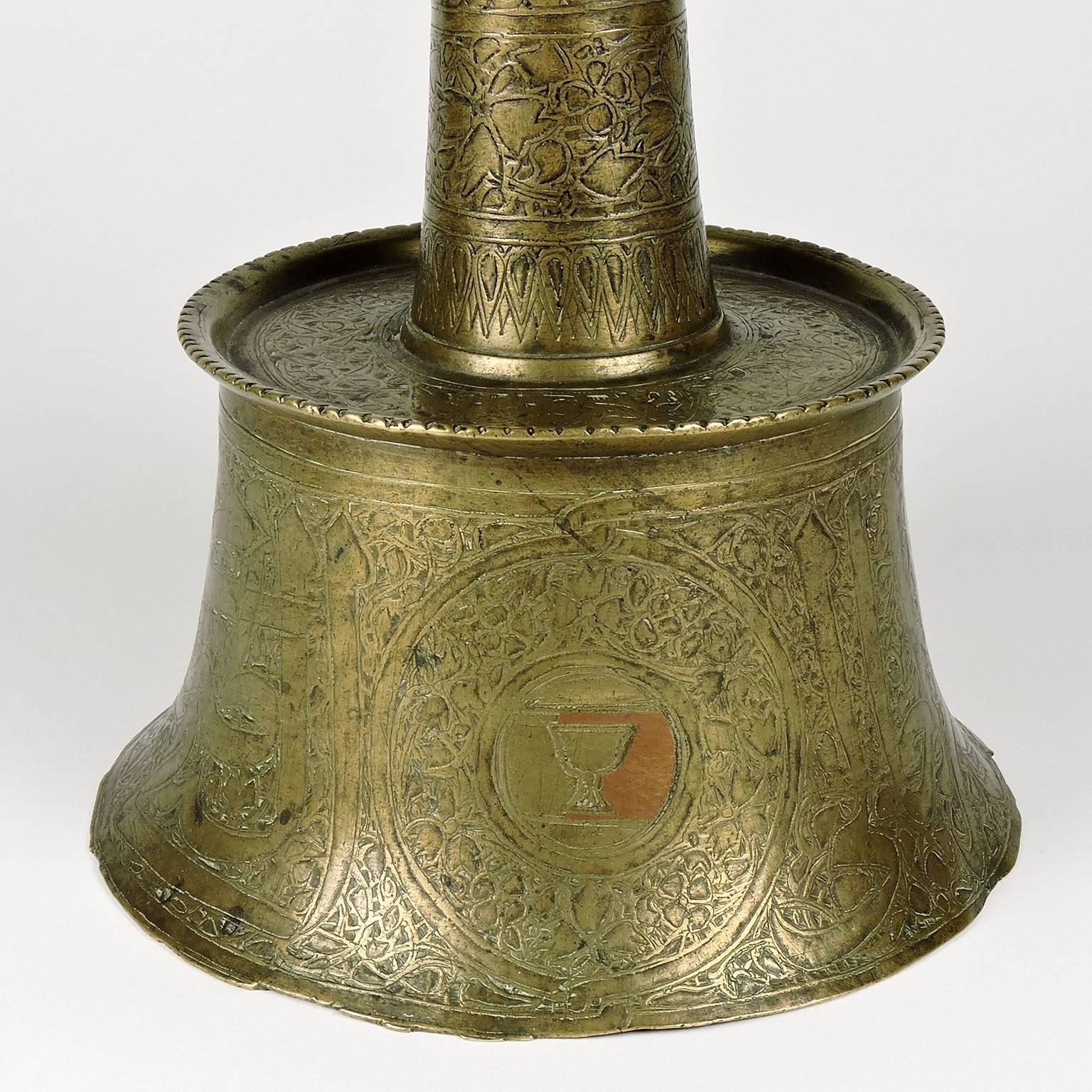 Egyptian Mamluk calligraphic brass candlestick, 14th century. The base of waisted form leading to slightly reduced foot, cylindrical neck tapering to inverted mouth surmounting a short drip pan. Base with a large band of thuluth calligraphy against