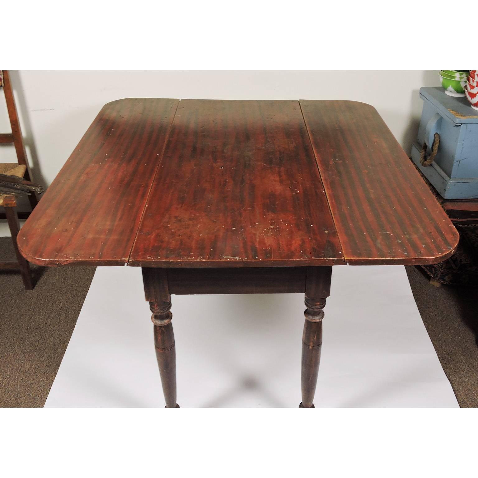 American country Sheraton grain painted drop-leaf table, with red ground and black grain decoration; swing out supports and turned legs. From Maine.
Dimensions: 29 1/4 x 41 3/4 x 20 1/4 inches (open: 40 5/8 inches).

 
