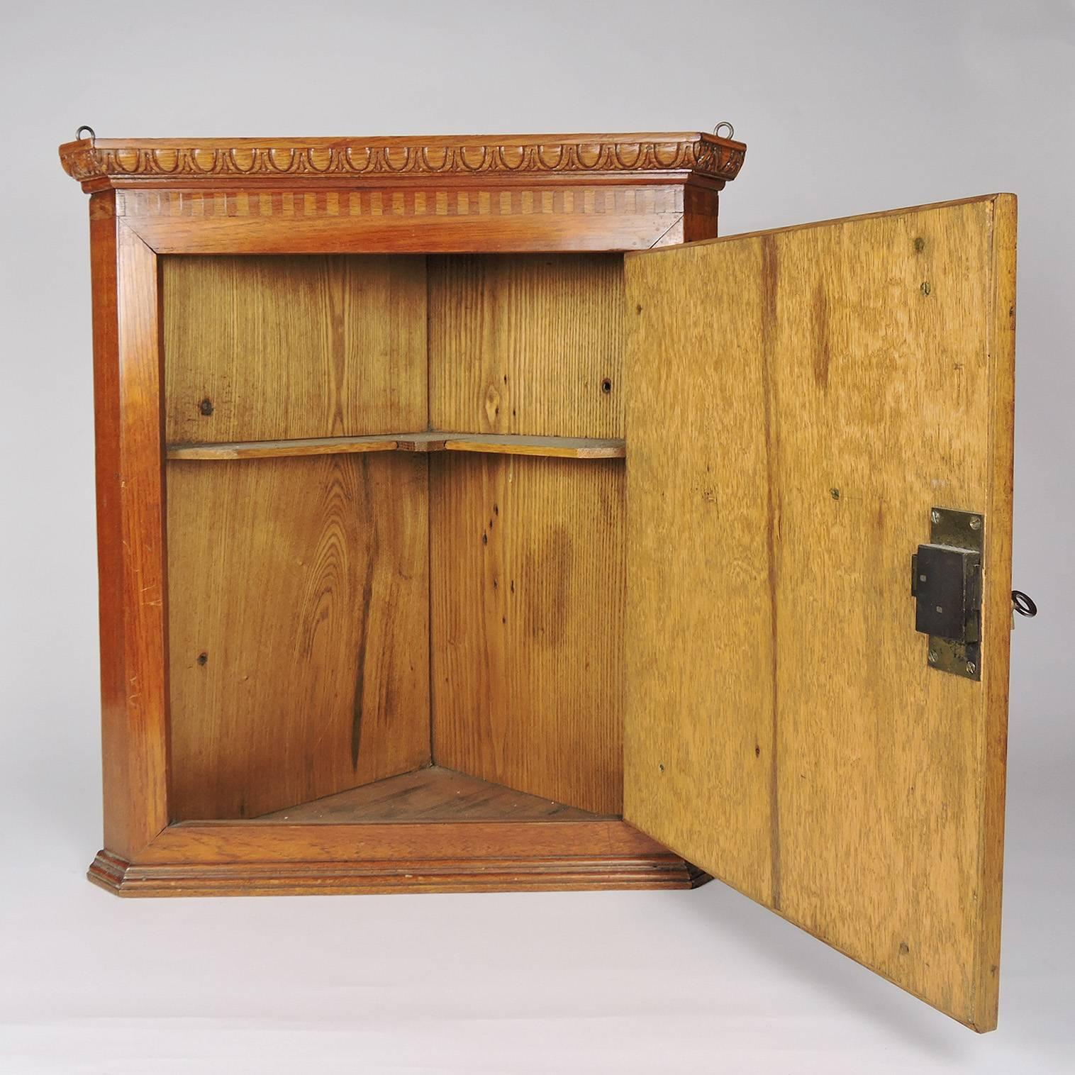 19th century Georgian oak and parquetry fruitwood inlaid hanging corner cabinet, with open interior and locking mechanism. Includes original key.
Dimensions: 19 1/4 x 13 3/4 x 10 inches.

 