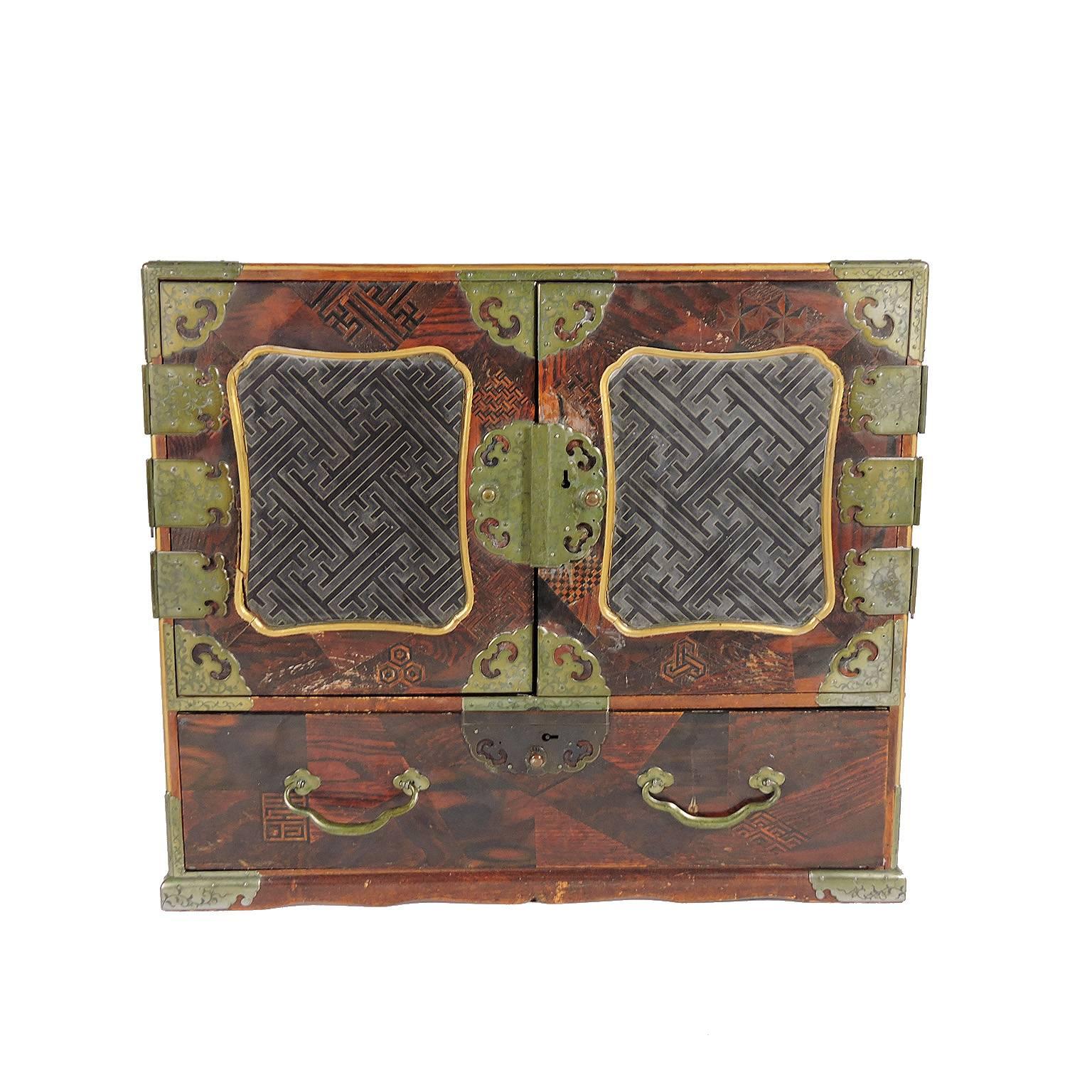A handsome 19th century Chinese inlaid rosewood and brass bound jewelry chest, with various inlaid designs and handles on each side with inset lacquer geometric design panels. Comprised of a single drawer below two doors opening to reveal a black