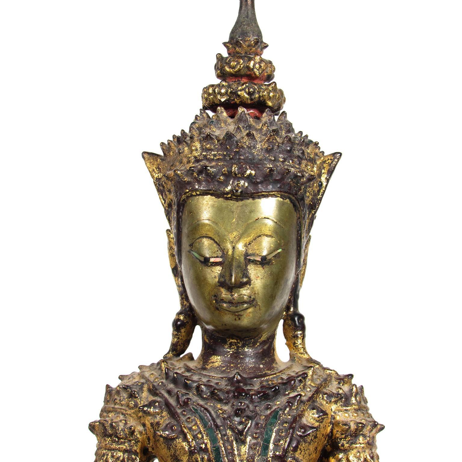 Antique gilt bronze statue of Thai version of Buddha. Figure seated on a lotus with a double cushion base, inset with colored green glass panels and remnants of red paint. With reliquary top. Provenance available to buyer. Measures: Height 23 in.
