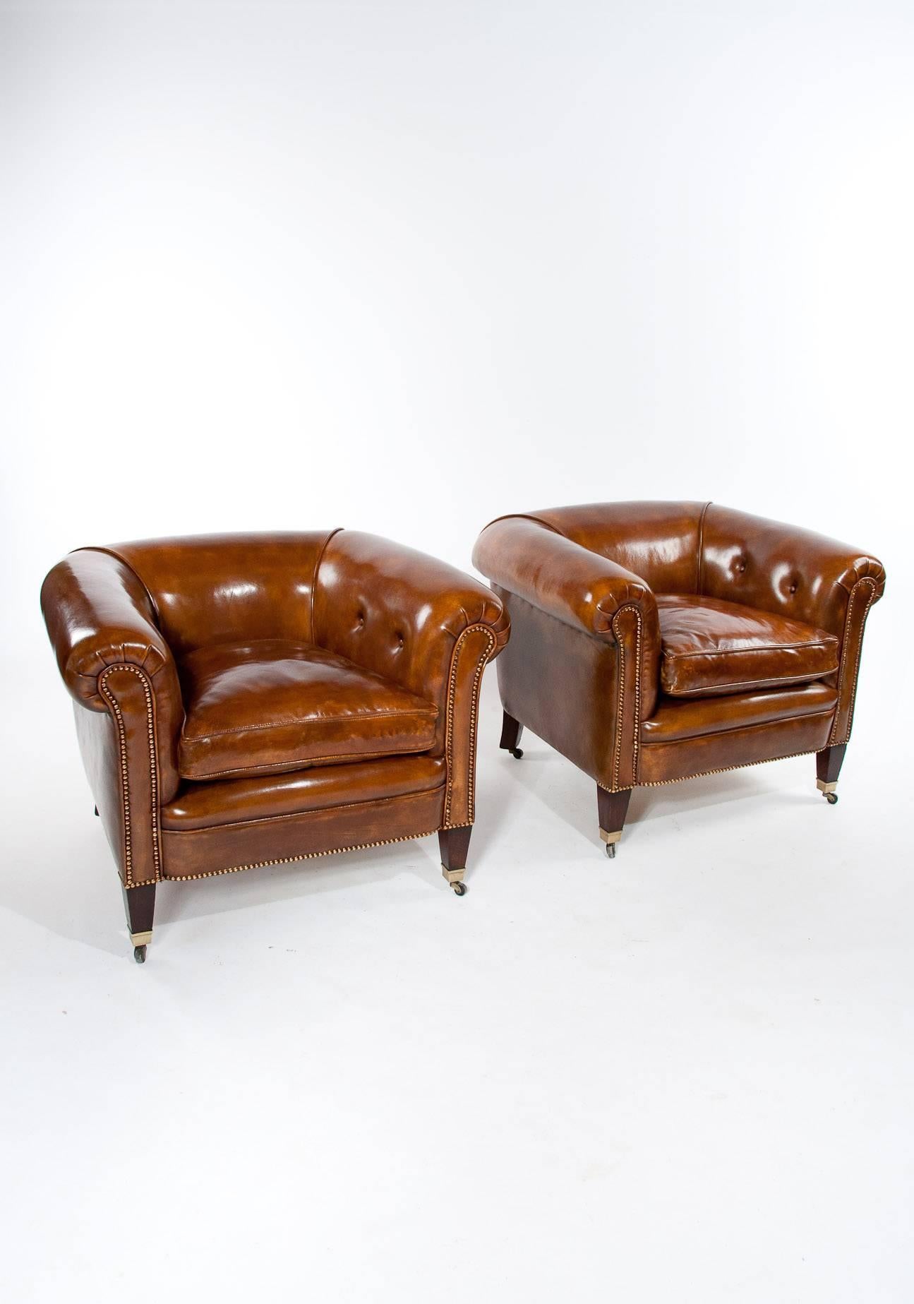 A very good quality pair of antique leather tub armchairs dating to circa 1910s-1920s. 

This rare pair of tub shaped armchairs have been upholstered in a fine quality hand dyed tan leather having shallow buttoned sides and deep feather down