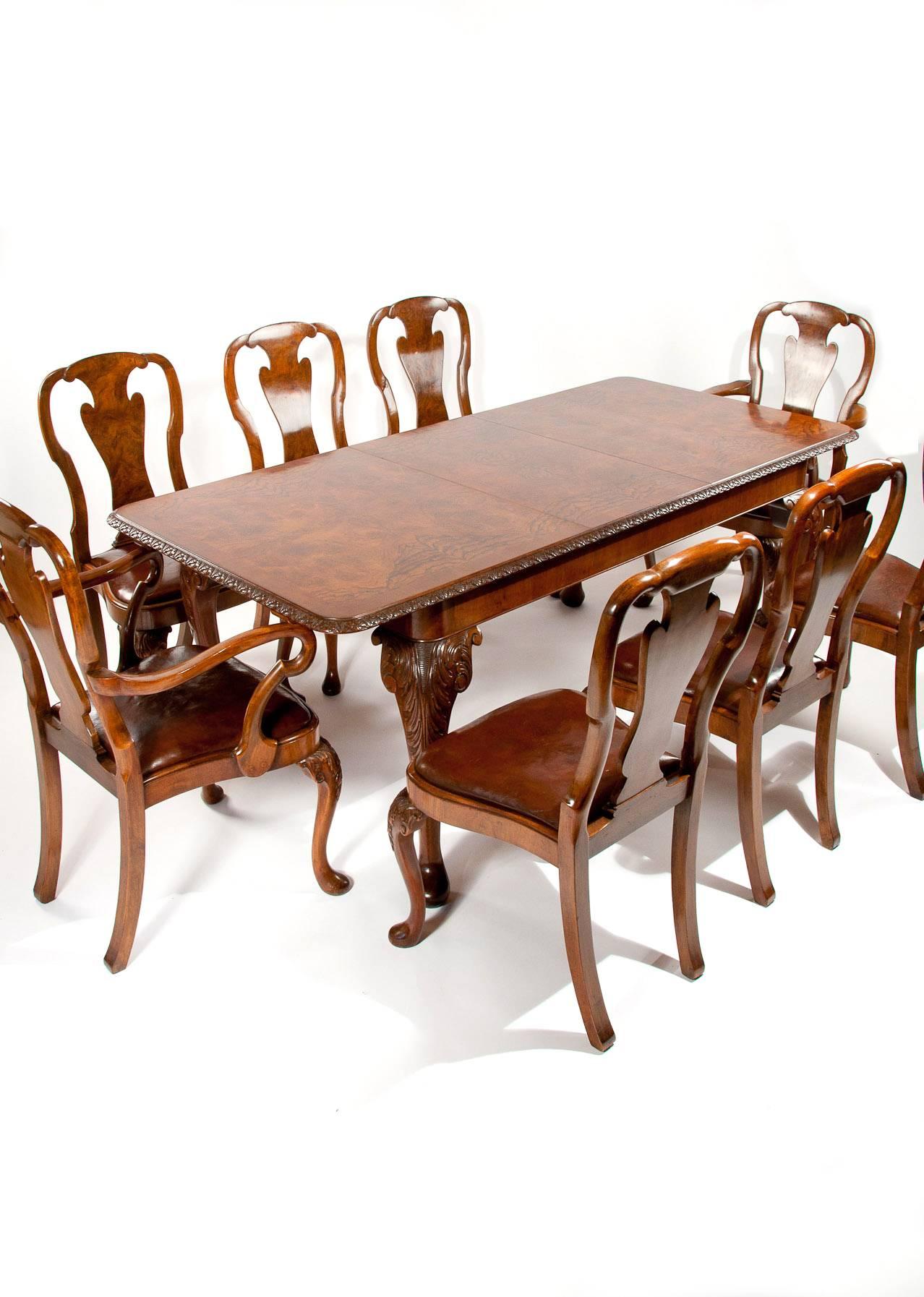 A very good quality antique walnut dining table and set of eight leather upholstered dining chairs.
This quality antique Queen Anne style dining table set dating to the 1920s consists of a large one leaf burl walnut cabriole legged dining table