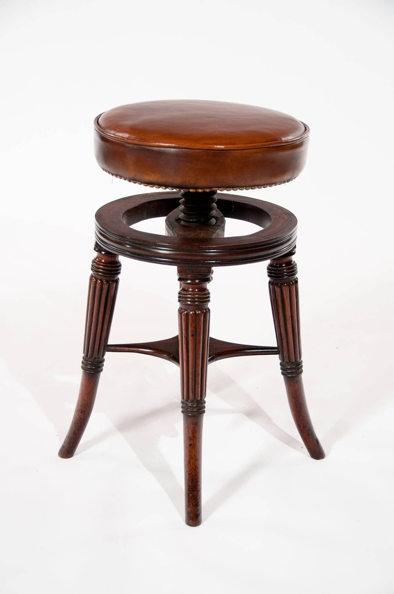 A fine quality regency piano stool having an adjustable leather upholstered seat.
The circular tan leather seat being fully adjustable by simply turning to the required height which is supported by four of the most elegant turned and reeded legs