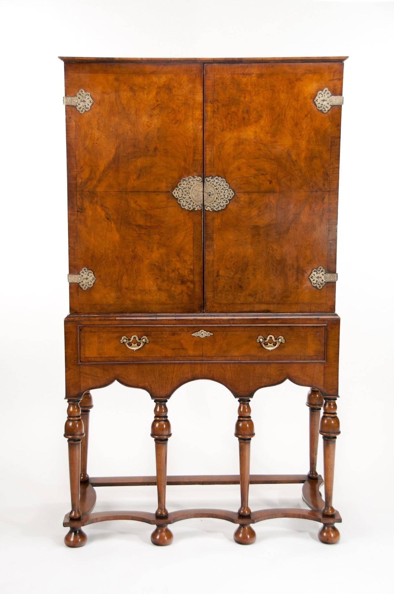 A good quality antique William and Mary style walnut cocktail cabinet dating to the early 1900s.
This quality cocktail cabinet has been constructed in the William and Mary style having a pair of walnut bookmatch veneered doors with crossbanded