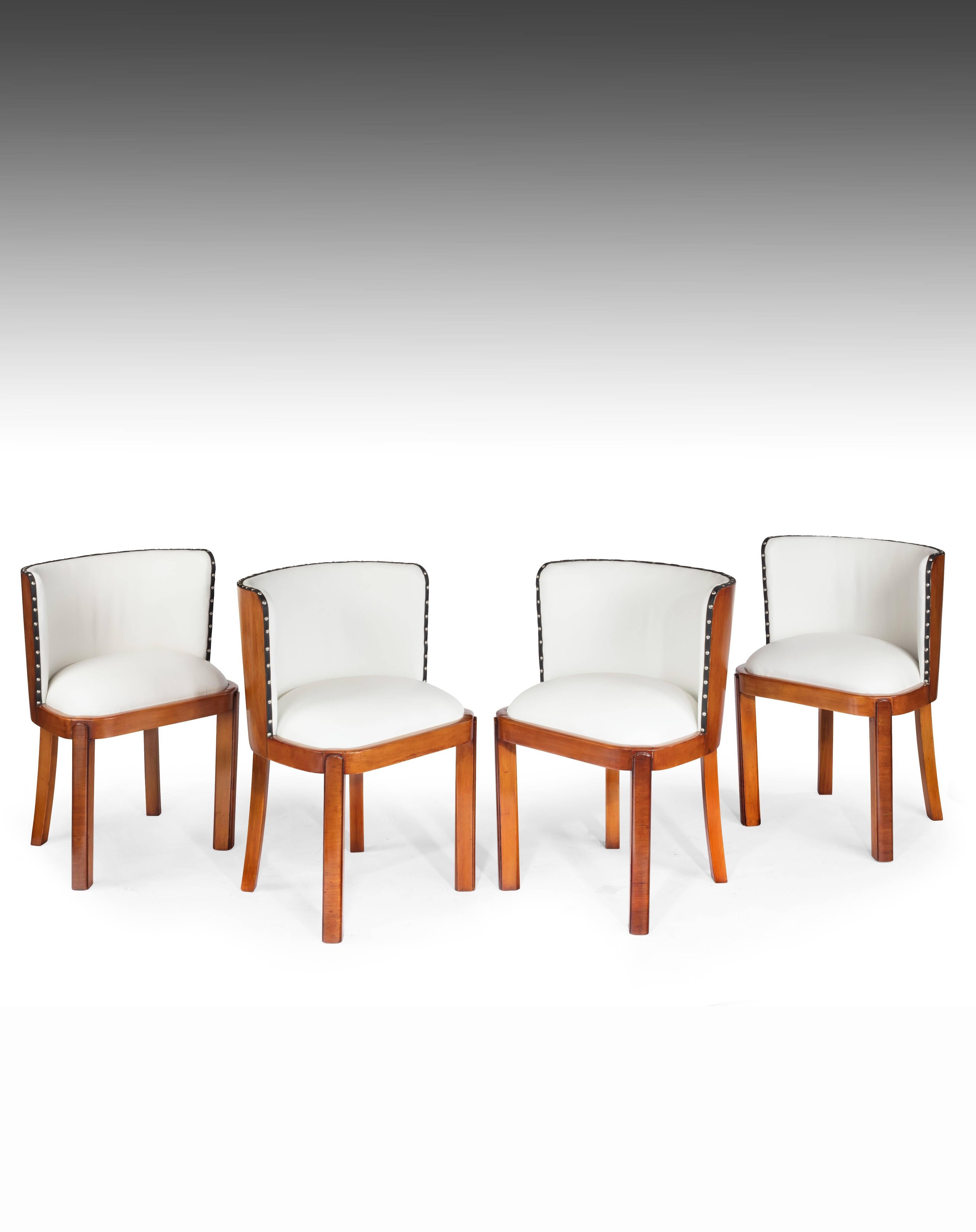 A very stylish set of four walnut white leather upholstered Art Deco shaped dining chairs.
This set of four very unique Art Deco dining chairs have walnut veneered tub shaped backs which are upholstered in a Fine quality white leather hide with a