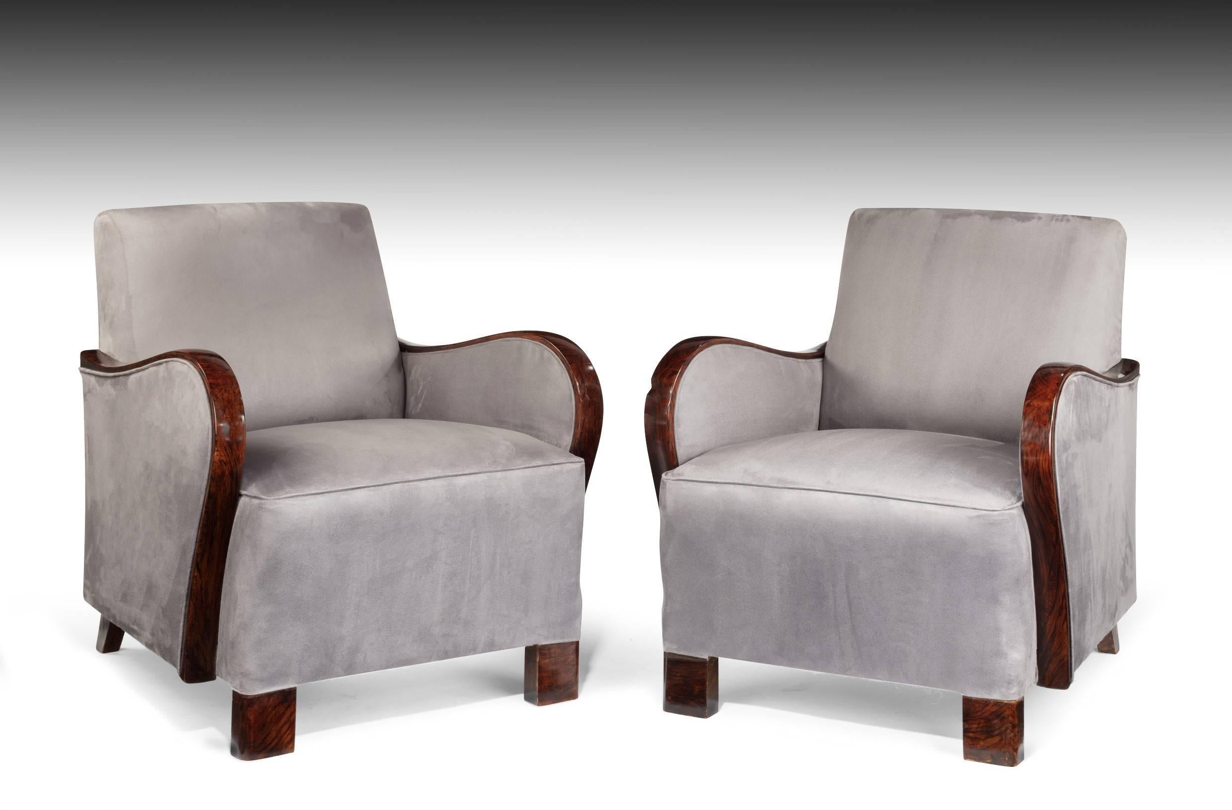 A good pair of Art Deco armchairs with faux rosewood arms upholstered in a steel faux suede fabric. 
Having square backs with sprung seats this pair of armchairs date to circa 1930. The faux rosewood arms are shaped and polished to a piano like