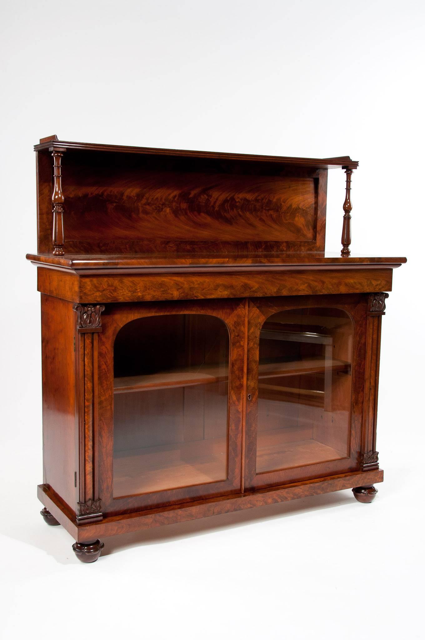 A superb quality William IV mahogany two door chiffonier. This chiffonier dating to, circa 1835 has been constructed to the finest quality with stunning flame mahogany veneers having a raised tier with central panelled back supported by turned