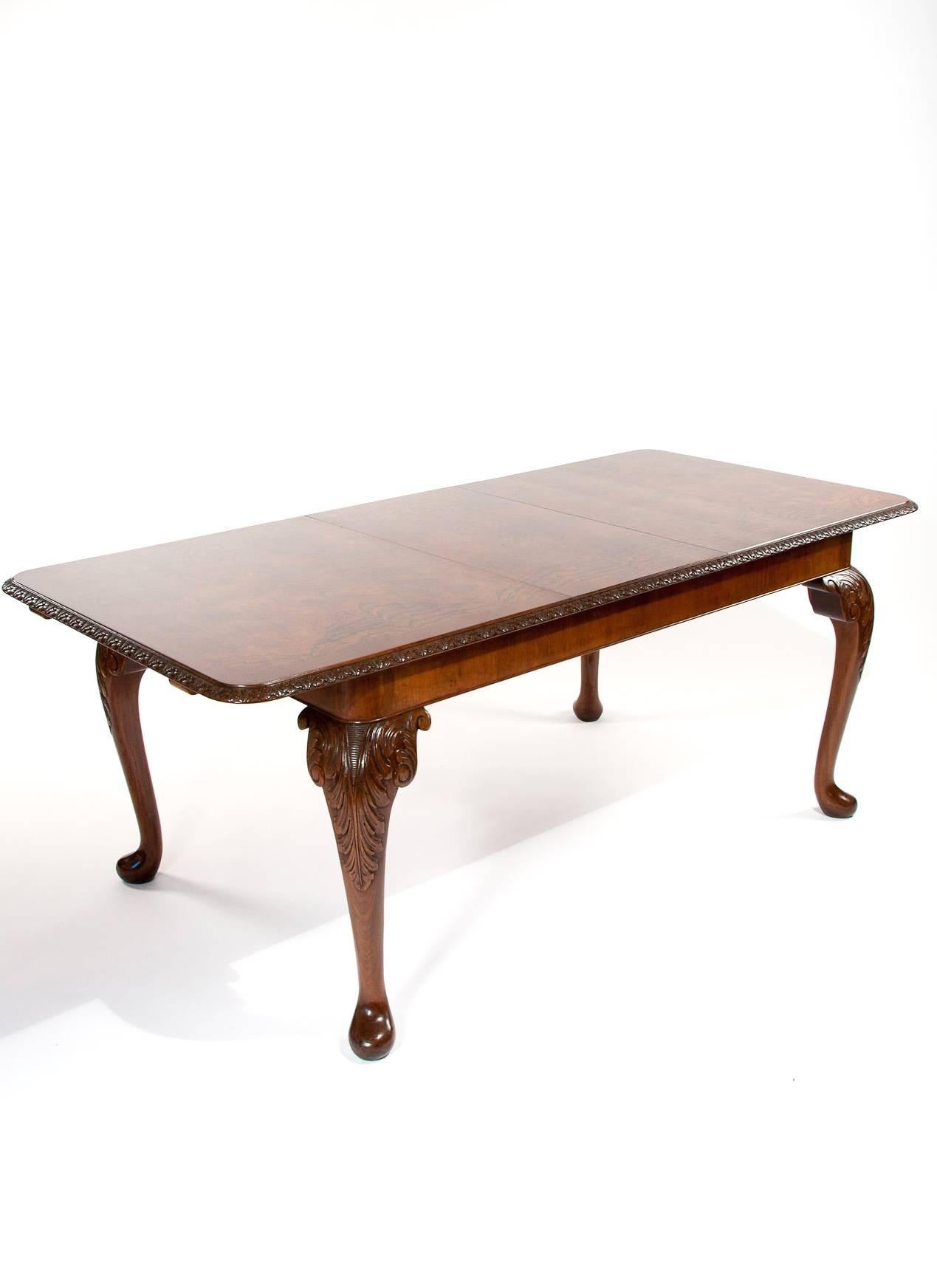 A quality antique burr walnut extending dining table with extra leaf standing on cabriole legs.
This quality antique Queen Anne style dining table dating to the 1920s has a rectangle burr walnut quarter bookmatch veneered top with a crossbanded