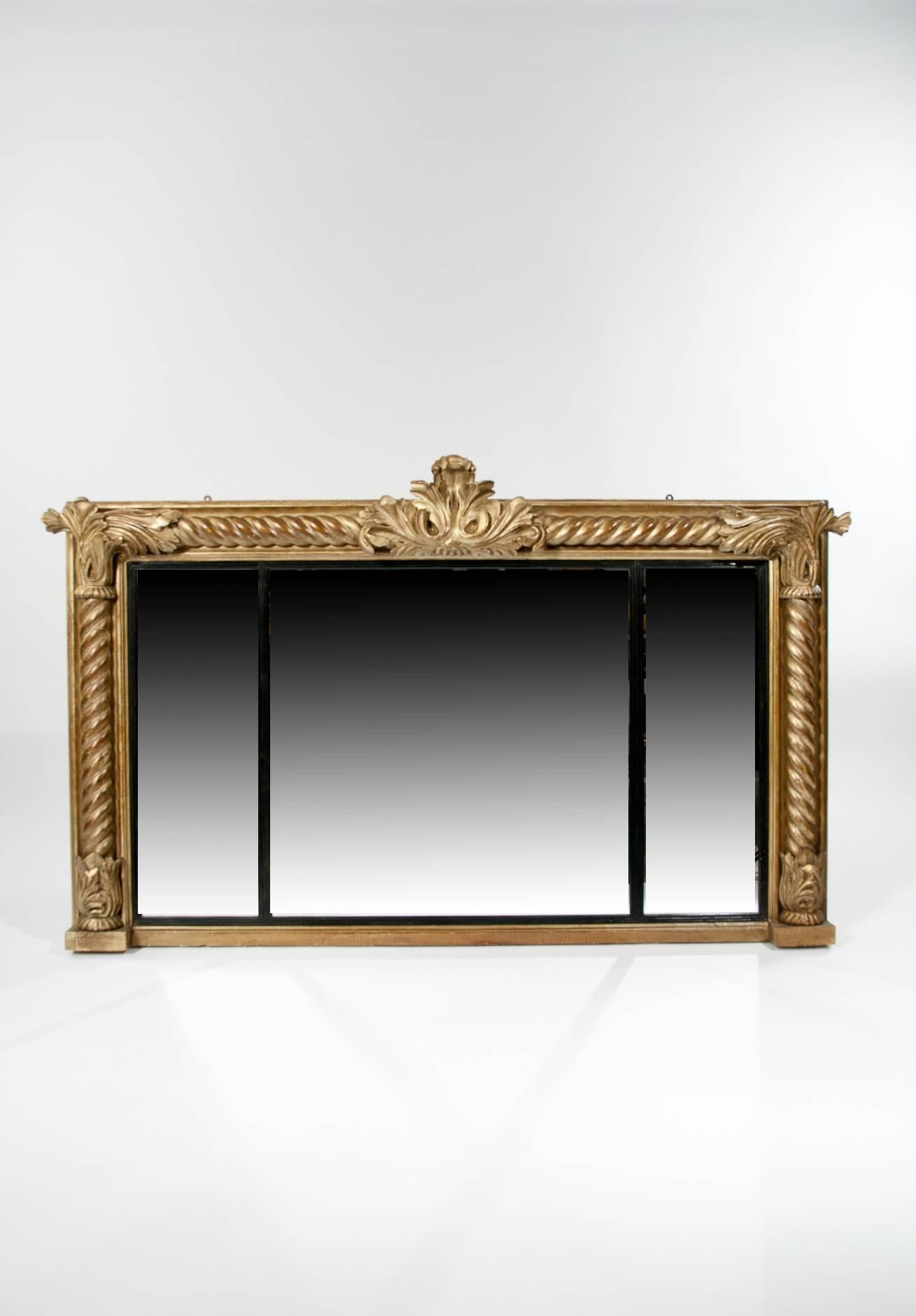 A very good quality and ornately carved giltwood framed Regency overmantle mirror with a three section glass plate. 
The gilt frame having carved reeded, twisted columns with acanthus leaf design to all four corners and a central foliage cartouche.