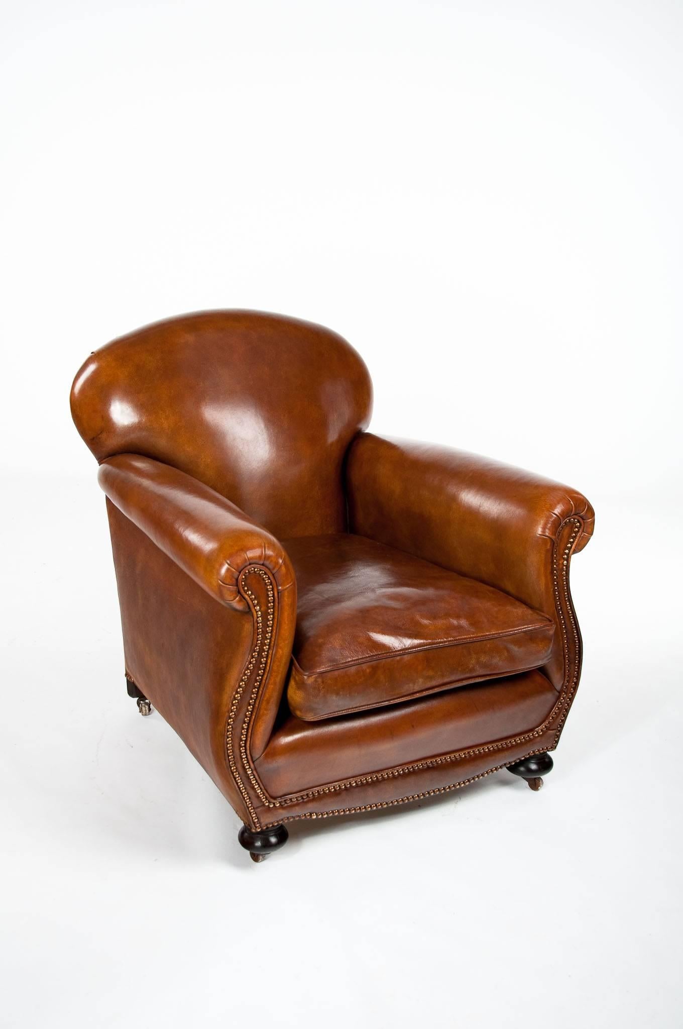 A Quality antique leather upholstered club armchair.

 This Victorian leather upholstered club armchair has a rounded back with beautifully serpentine shaped arms and brass nailed studding. The leather chair has a generous feather cushioned squab