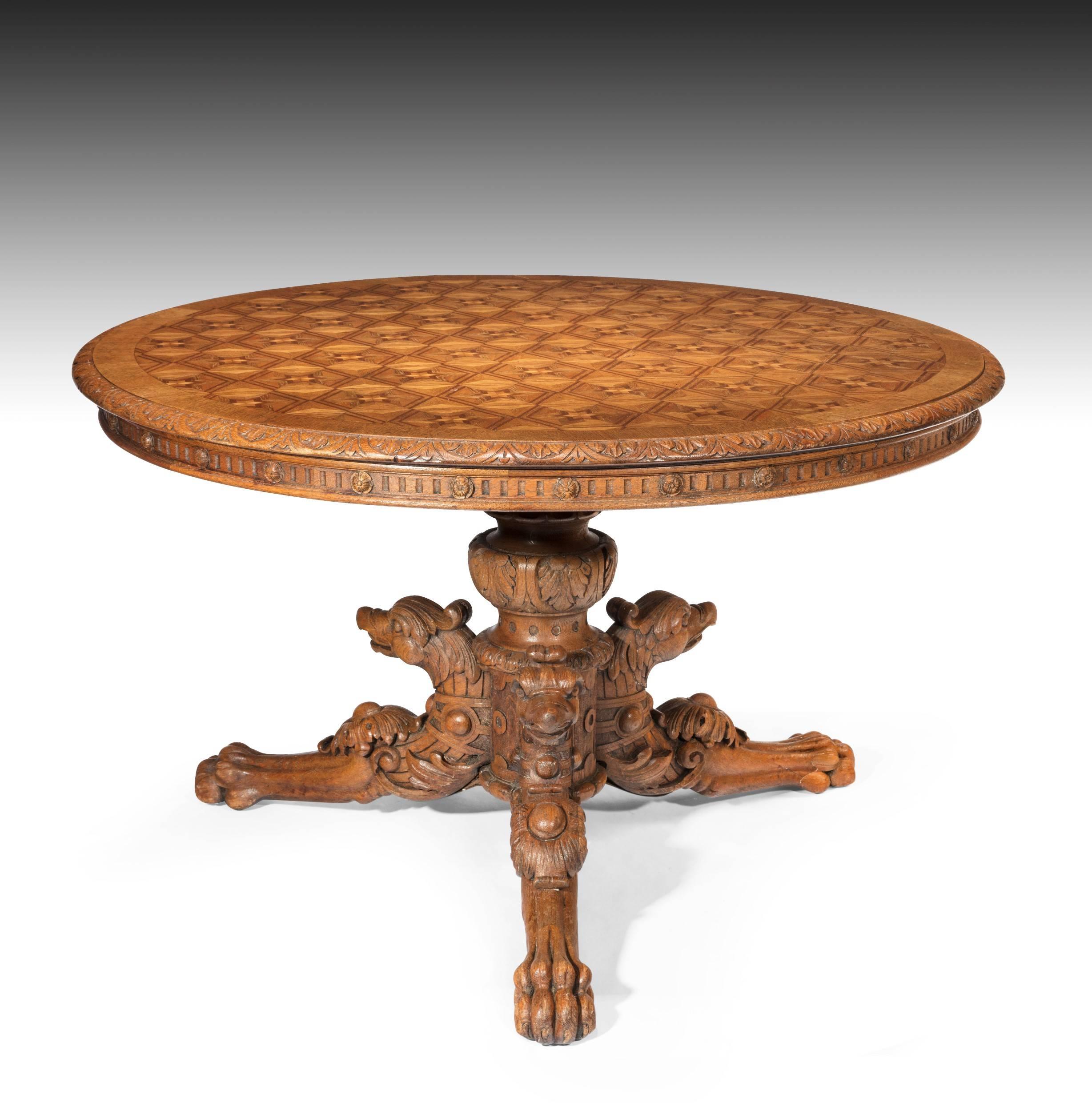 A wonderful and rare circular oak parquetry inlaid tilt-top table on carved griffon base.
The large oak circular top being inlaid with a repeated 'trompe l'oeil' star motif with a carved foliate edge having a fluted frieze with rosettes above a