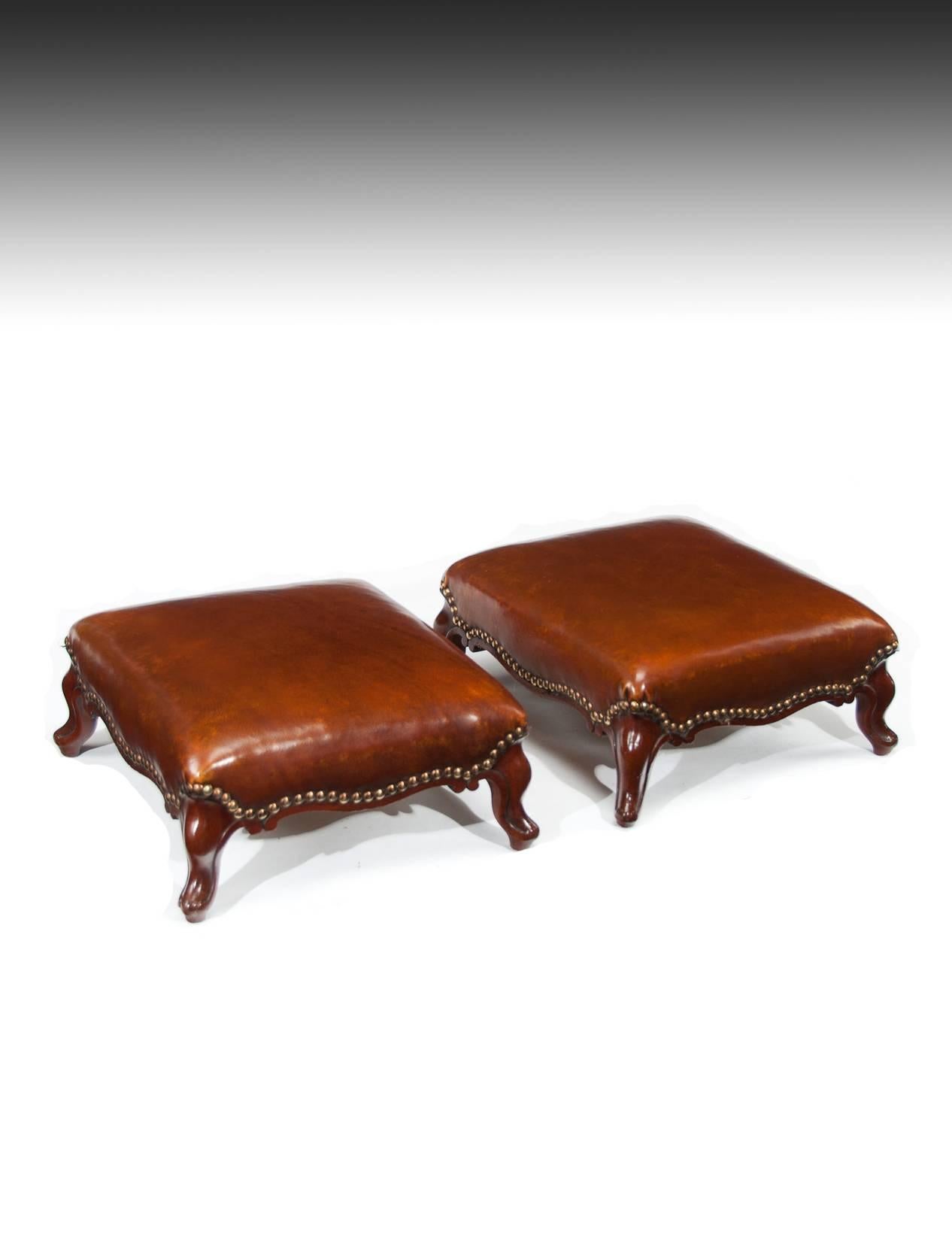 A good pair of leather upholstered Victorian mahogany footstools.
This pair of Victorian footstools date to circa 1870 and have been newly upholstered in a fine quality hand dyed leather hyde with a brass nail surround finish. 
Raised on shaped