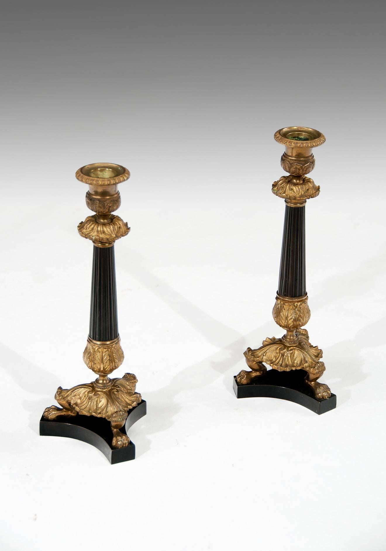 Very attractive and fine quality pair of patinated bronze and ormolu candlesticks on concave tri-form bases raised on foliate cast lion paw feet. Having fine cast urn shaped nozzles with removable bobeches supported by a tapering reeded patinated