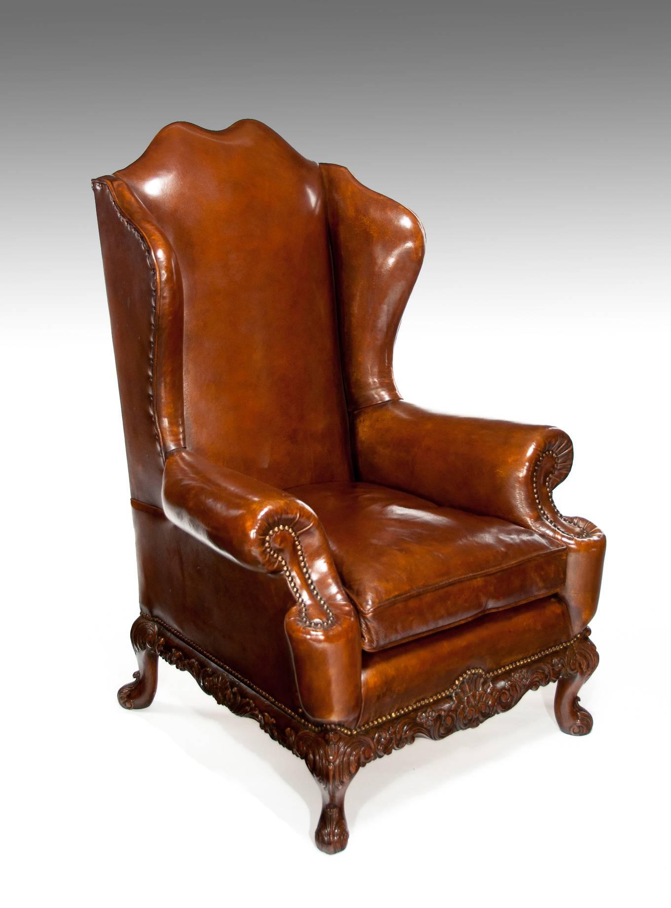 A very good quality and well-proportioned leather upholstered carved walnut wing chair, circa 1920s
Having a camel shaped back flanked by out swept winged sides which concave to join the outward scrolling armrests, having brass studwork nailing and