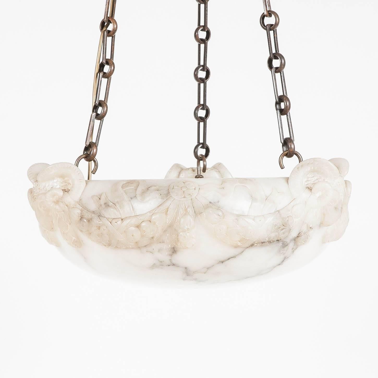 A 1920s white alabaster hanging light with carved ram's heads and floral swag decoration, with later bronze chains and ceiling rose.

Wired for electricity.