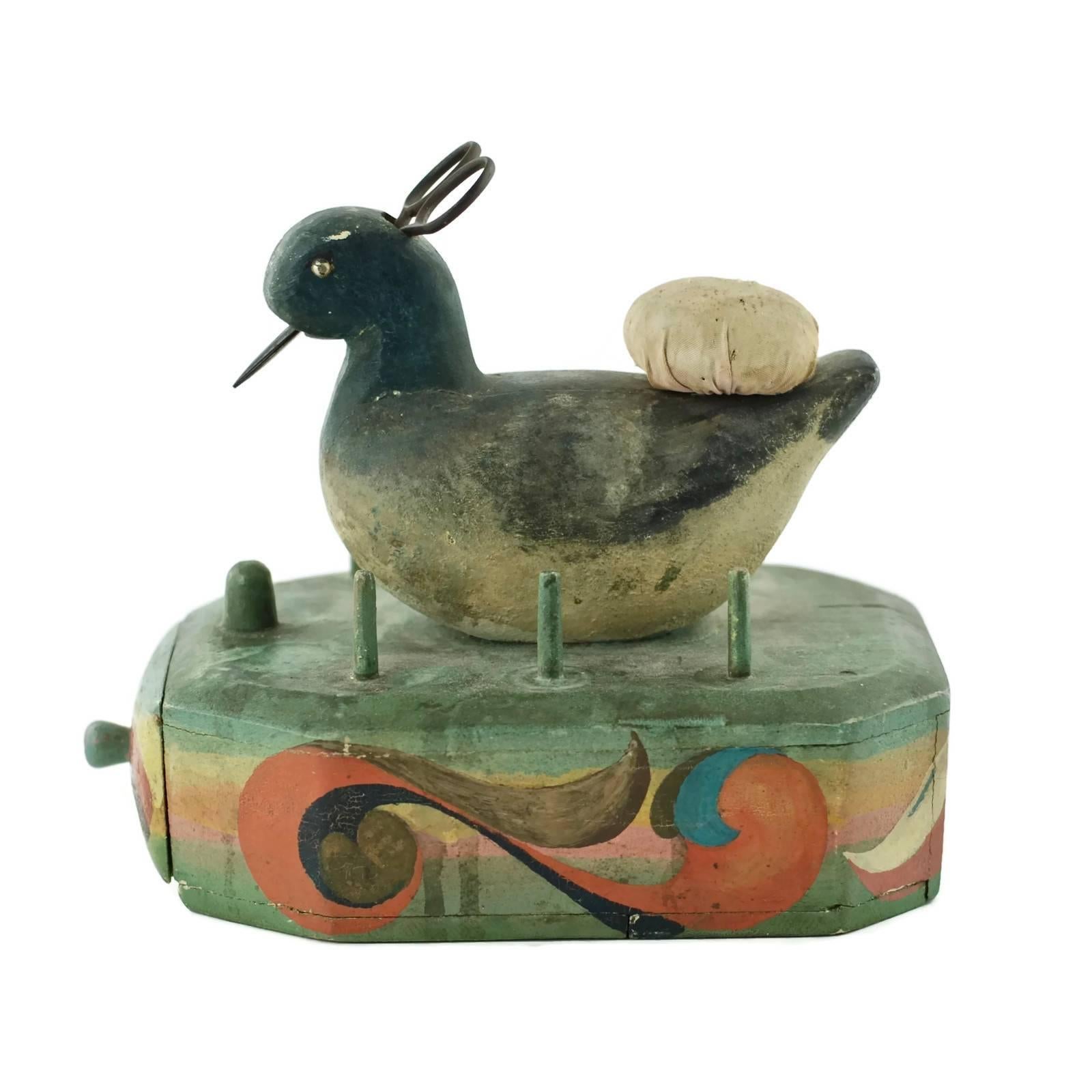 This charming 19th century hand-carved wood sewing caddy features a figural bird atop an octagonal base containing a single drawer. The top of the base has six dowels made to accommodate spools of thread and has a larger knob at the front to hold a