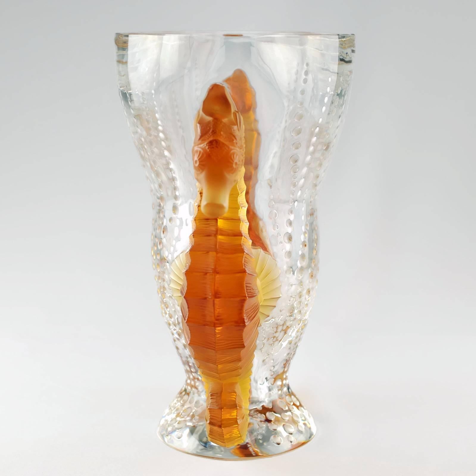 This substantial signed and numbered limited edition Lalique vase is titled Vase Poseidon and features a seahorse motif executed in amber crystal. The seahorses are quite large with highly detailed bodies which flank the clear crystal vessel. The