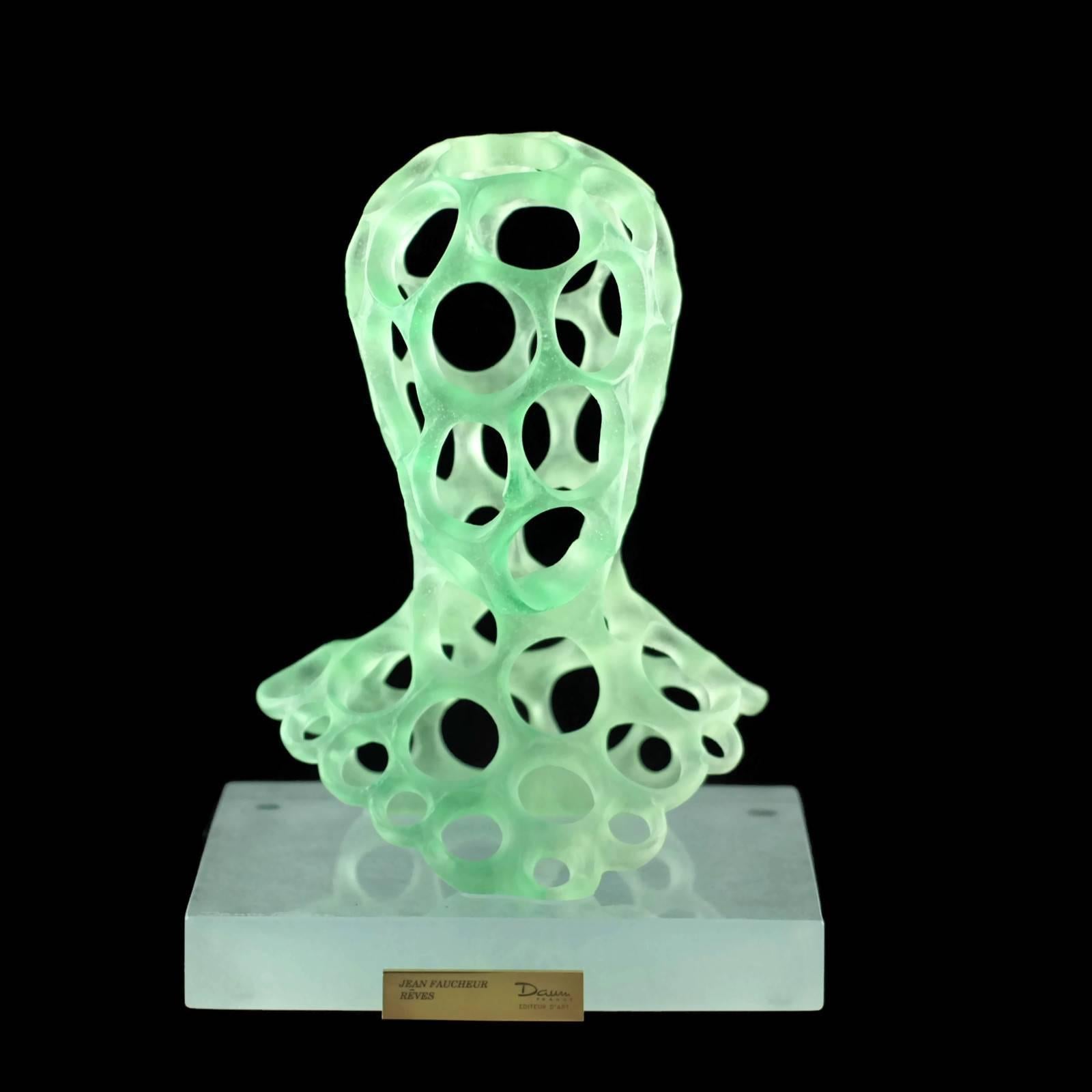 This signed and numbered limited edition pâte de verre sculpture was designed for Daum by French artist Jean Faucheur (b. 1956). The piece is titled Rêves - translated as Dreams - and depicts a stylized human head executed in translucent green pâte