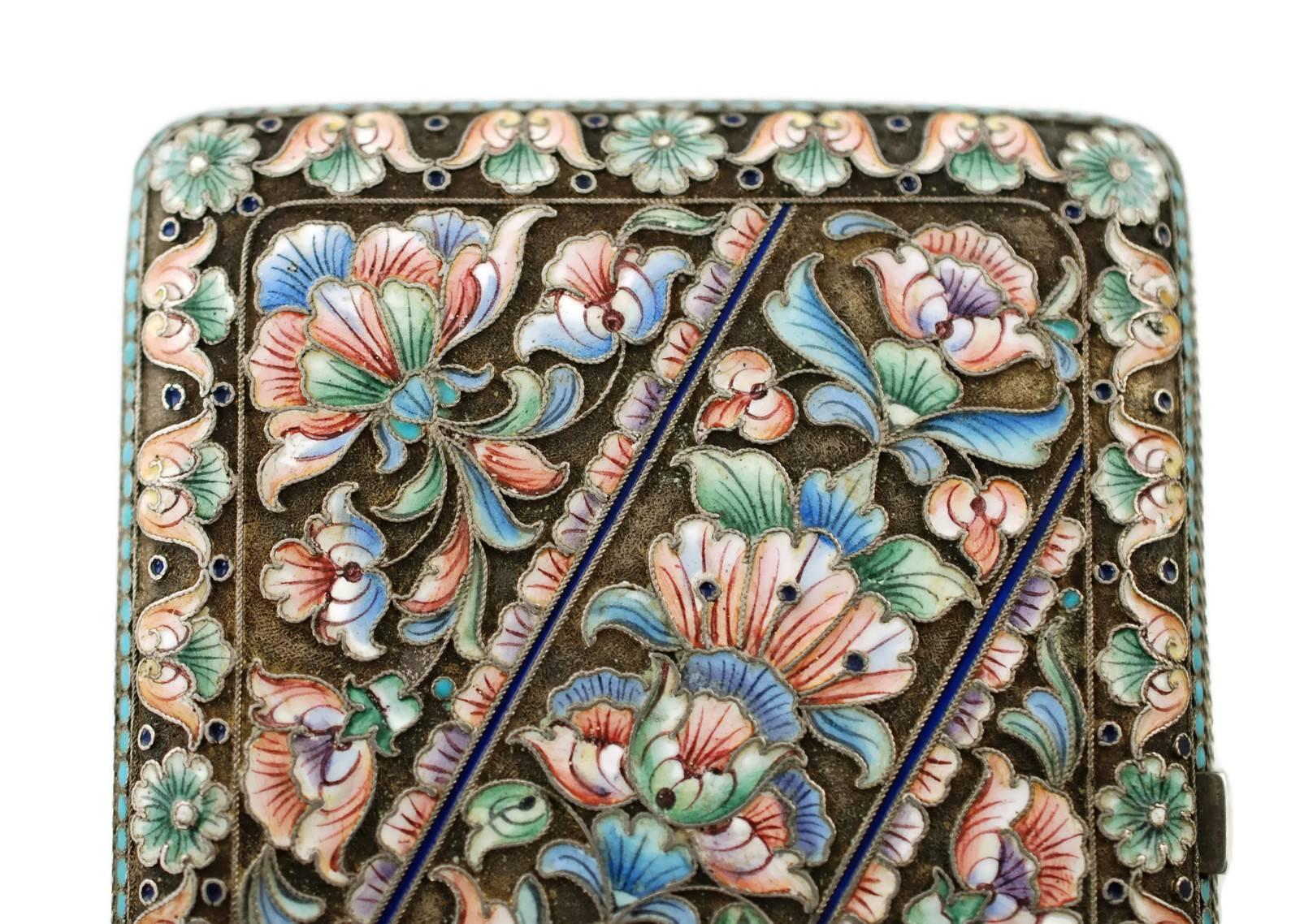 This elegant Russian Art Nouveau silver cigarette case has a rectangular form with rounded corners and features an ornate cloisonné enamel floral and foliate motif executed in shades of pink, blue and green with cobalt blue accents. The pattern is