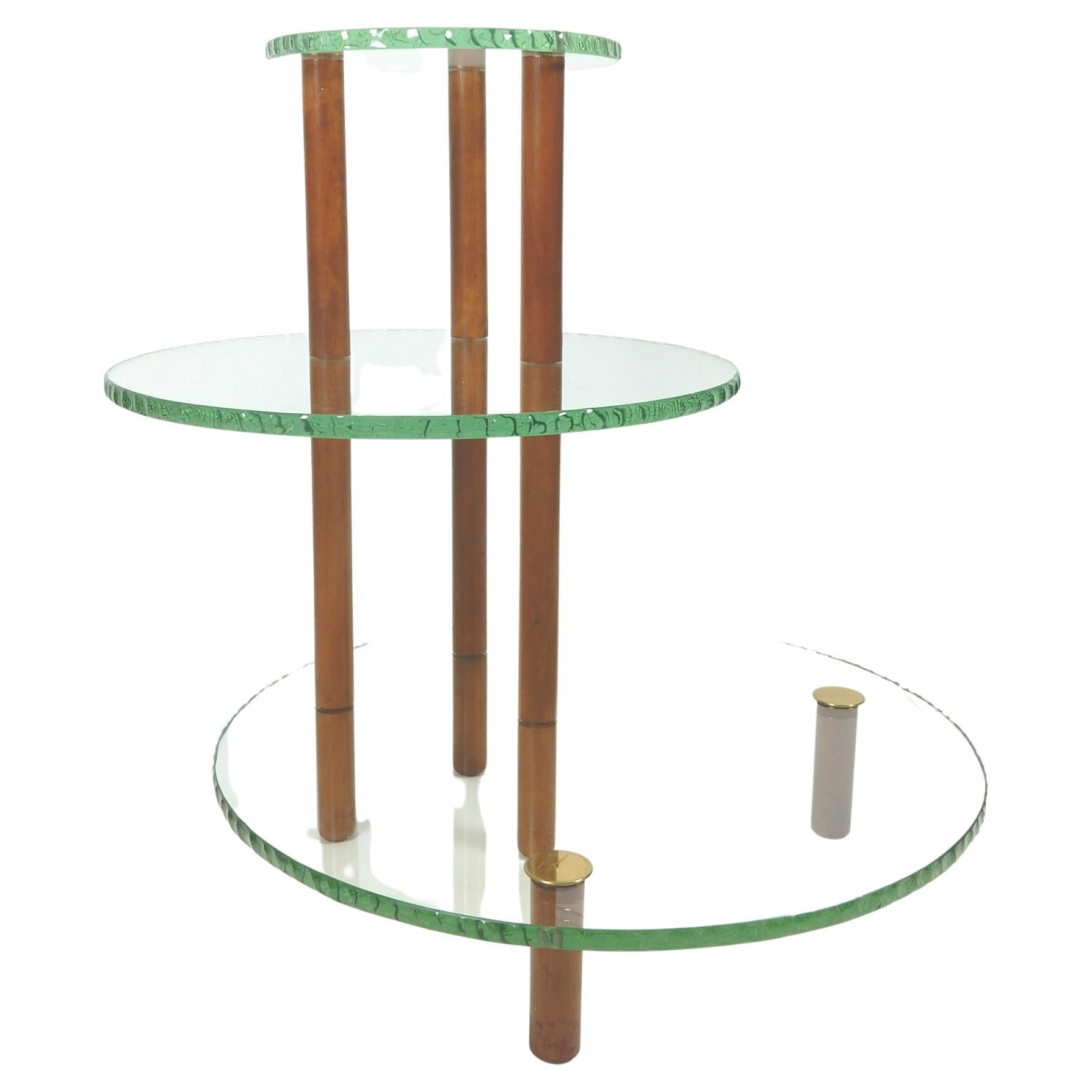 Gorgeous asymmetrical 3-tier etagere' table in the style of Fontana Arte', circa 1960s.
Chiseled green edge glass shelfs. 
Walnut dowels support legs topped with polished brass finials.
Would make a perfect dry bar or curio display.
Bottom glass