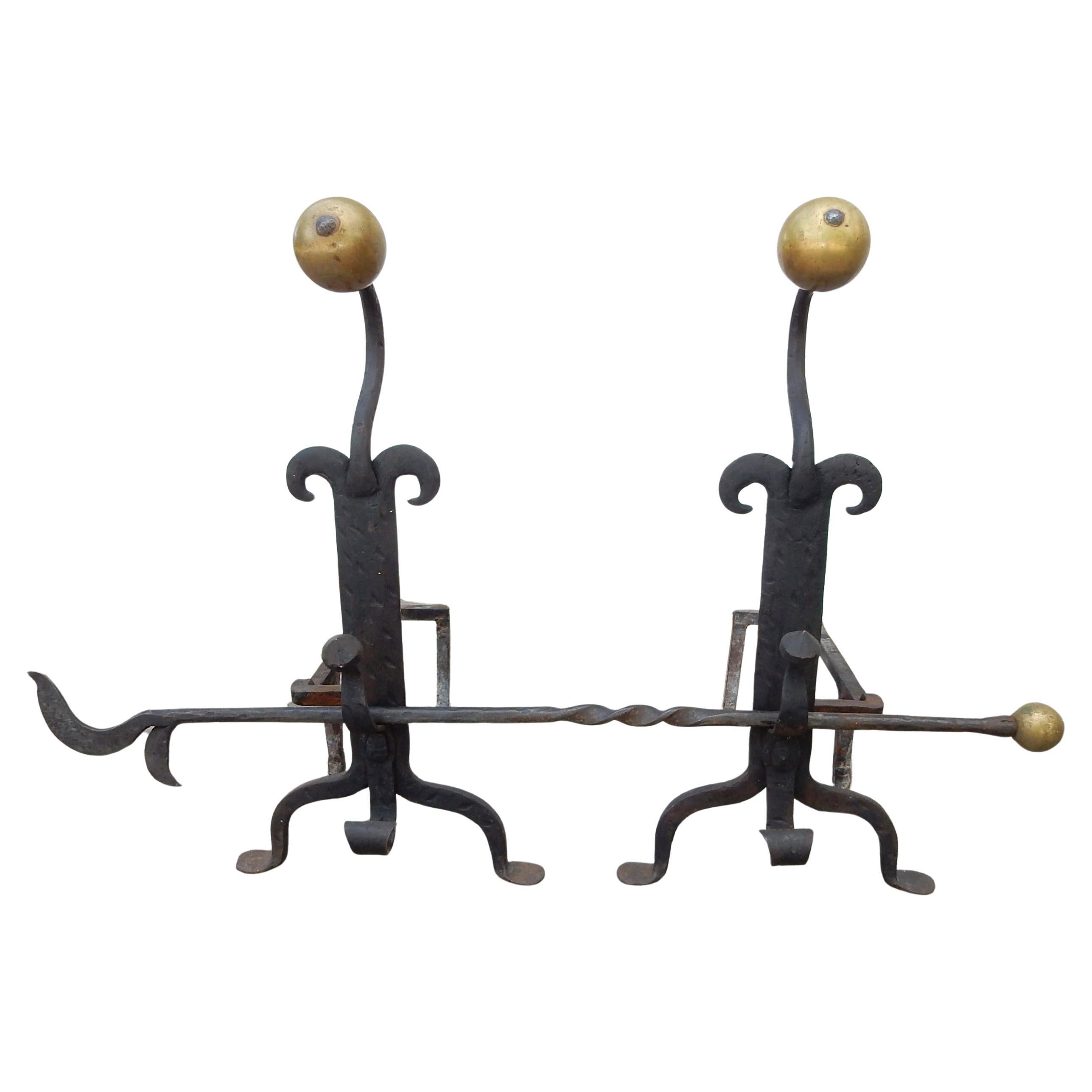 A pair of substantial Arts and Crafts artisan blacksmith-made andirons with matching tool set formed of wrought iron and formed brass ball handles. Andirons have scrolled spit supports standing on arched legs with penny feet. Log poker with twisted