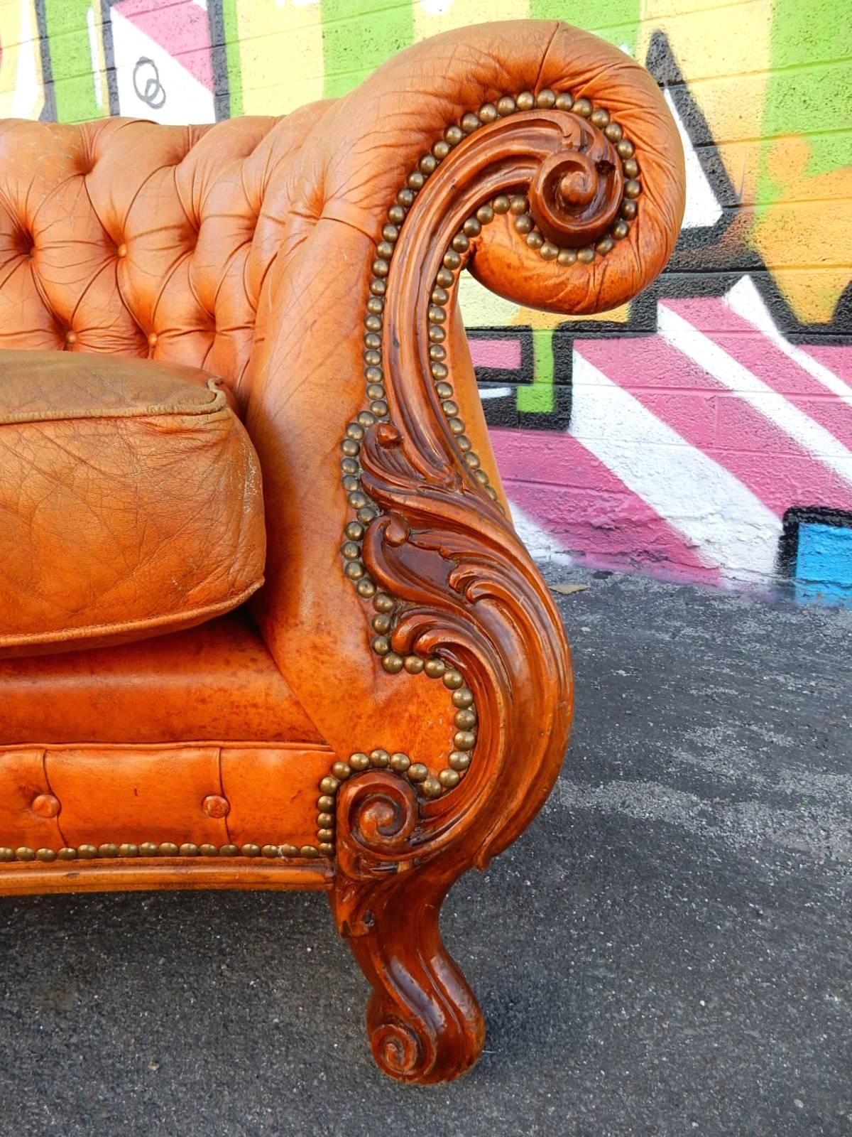 A Chesterfield sofa like no other. 
Supple marbled caramel leather & Naugahyde upholstery with beautifully hand carved scrolling detail on each side and legs.
 Aged brass tacks trim all edges.
The sitting area and tufted back leather is soft and