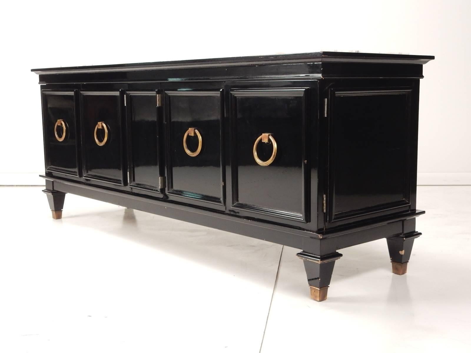 Gorgeous piece attributed to Dorothy Draper.   
Low, small scale with mirror black lacquer finish and three part white marble inlay top. 
Four door cabinet with large solid brass ring pull. Capped brass feet. Finished back. 
This shows less than