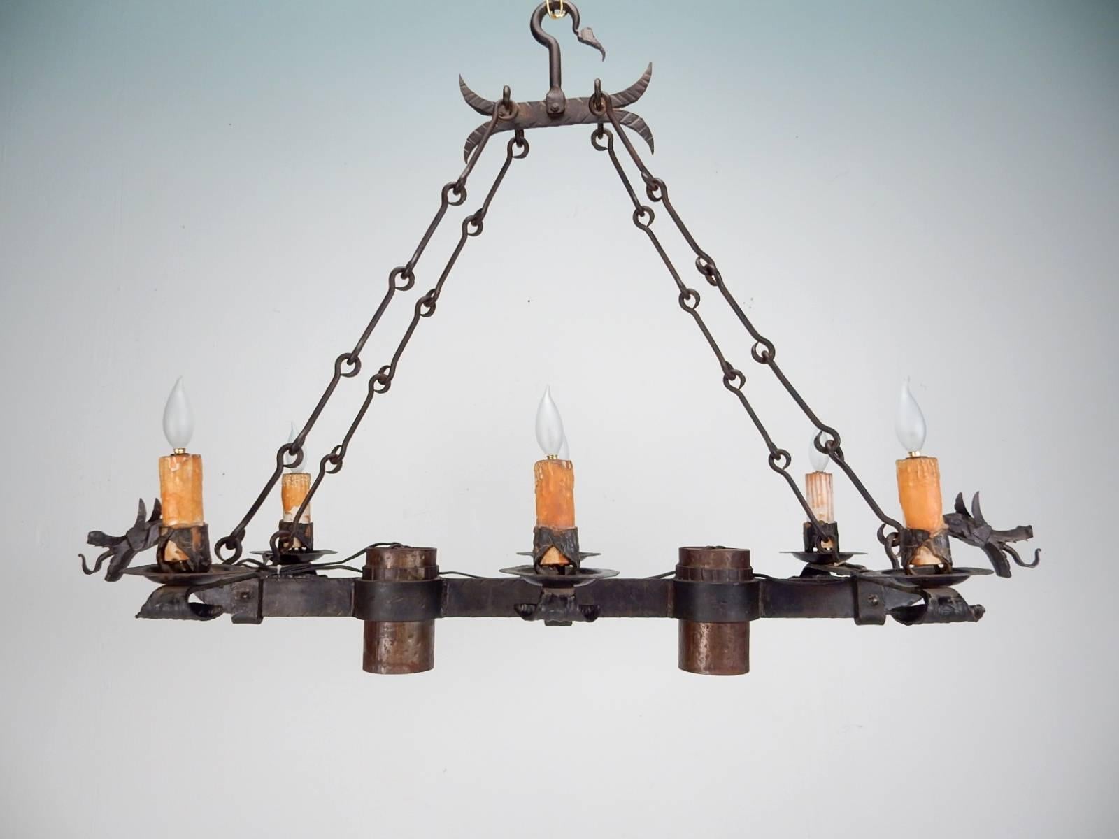 1930s Gothic wrought iron dragon Crémaillère chandelier.
Spectacular Medieval hand-forged iron dragons emanate from each end.
Over 4 feet long with four artistic link chains suspend from a large hook. 
Six candlestick bulbs on realistic wax