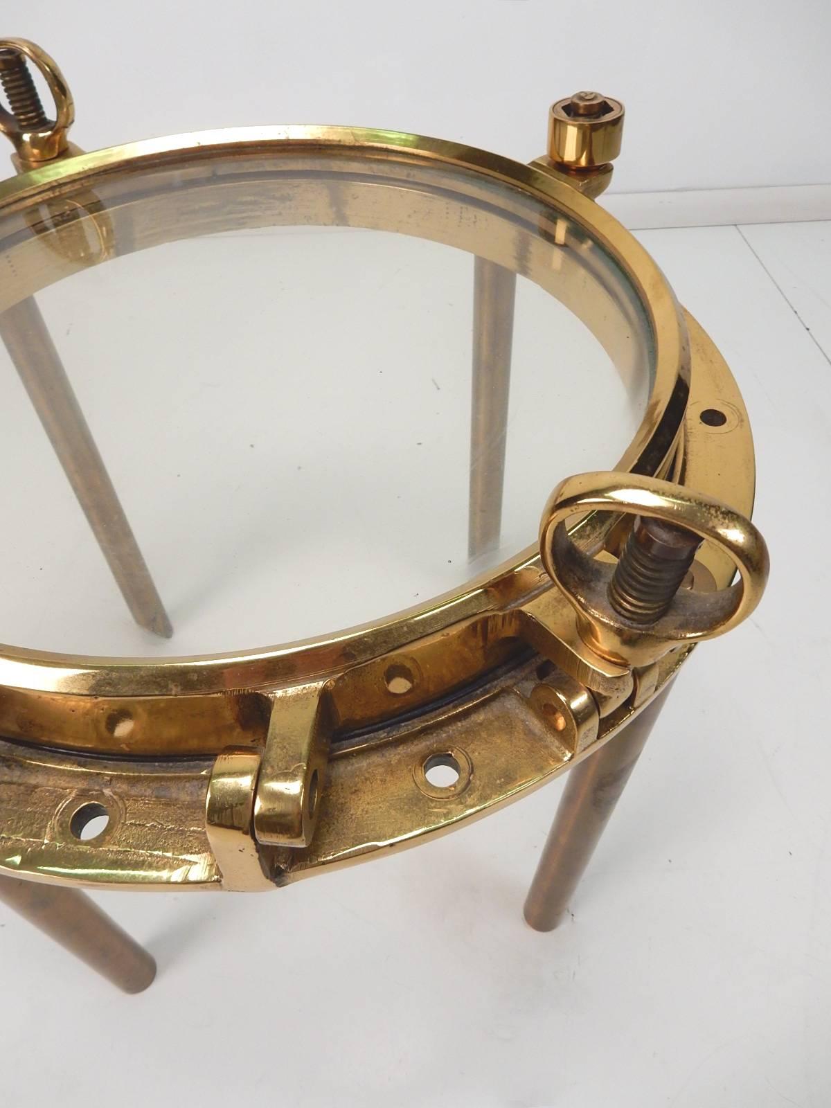 Marriage of a 1920s America brass ship porthole with four solid brass legs making a unique side table for an eclectic décor, circa 1970s.
Very heavy table of solid brass and thick glass.