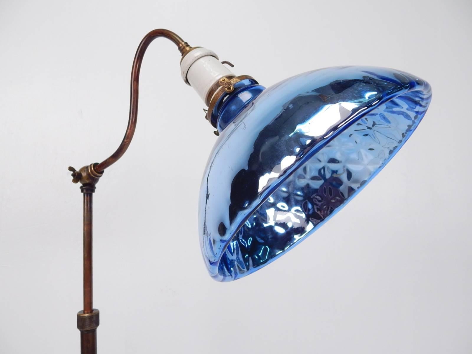 Blue mercury glass shade adjustable floor lamp, circa 1920s.
Porcelain socket, bronze and copper body with weighted lead base.
Raises and lowers via a knurled twist nut from 36 inch tall to 58 inch.
Shade arm adjusts via a wing nut knuckle.
Makes a