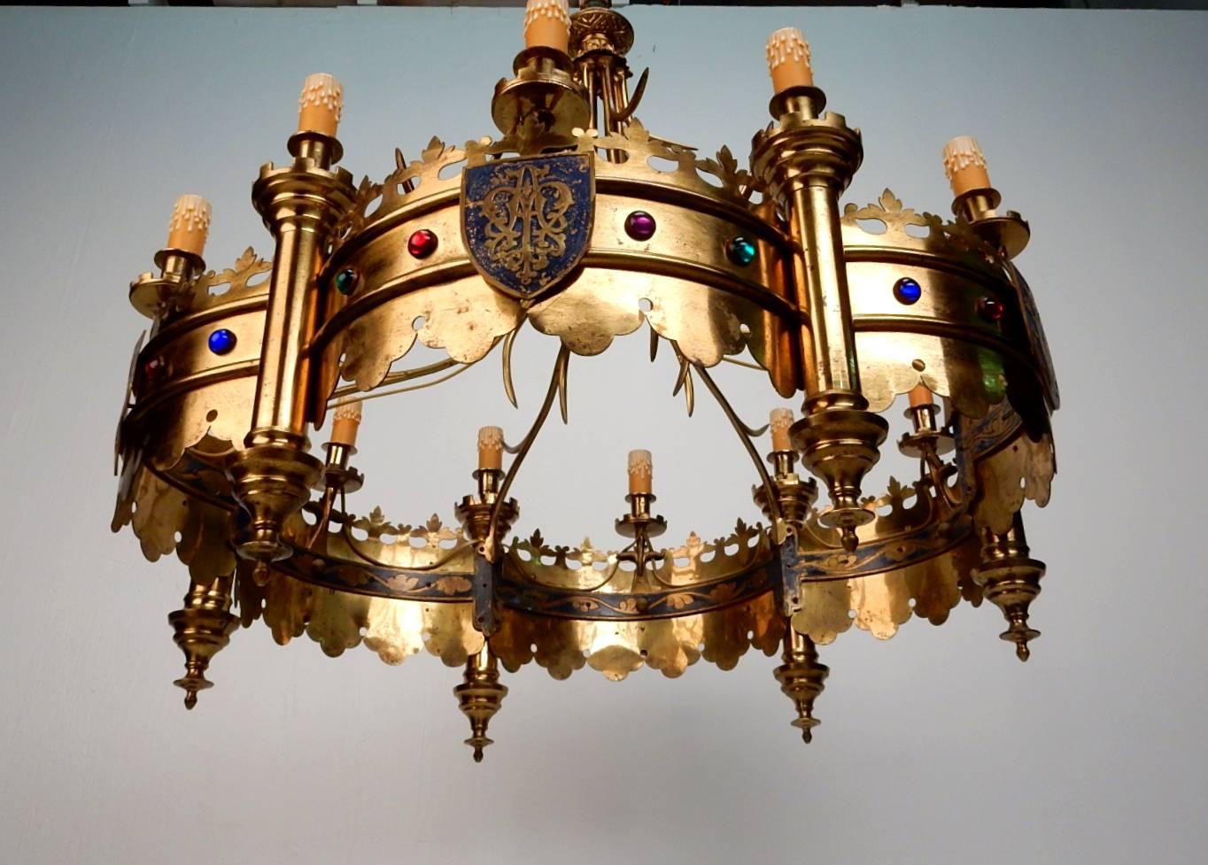 Incredible brass 12 bulb jeweled crown chandelier from France.
Heavy solid brass chandelier, hand formed with fantastic detail
including red, green and blue glass gems surrounding with enameled shields of flowers and design.
Began life as a