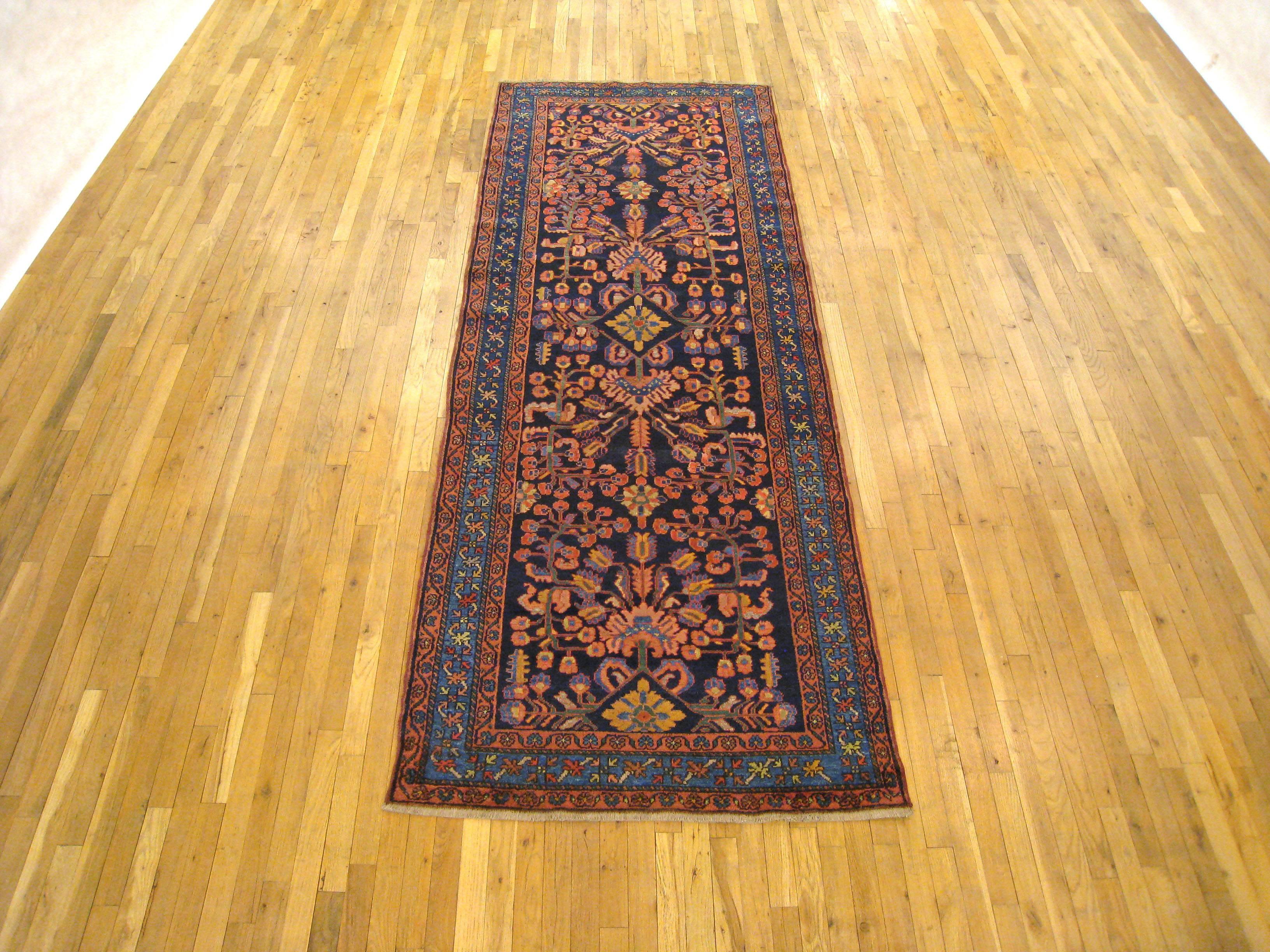 An antique Persian Hamadan oriental rug, circa 1920. Size: 10'2 x 3'8. This lovely hand-knotted rug is woven in a runner size, and is ideally suited for a hallway or gallery space. The field is characterized by a dynamic floral design in the dark