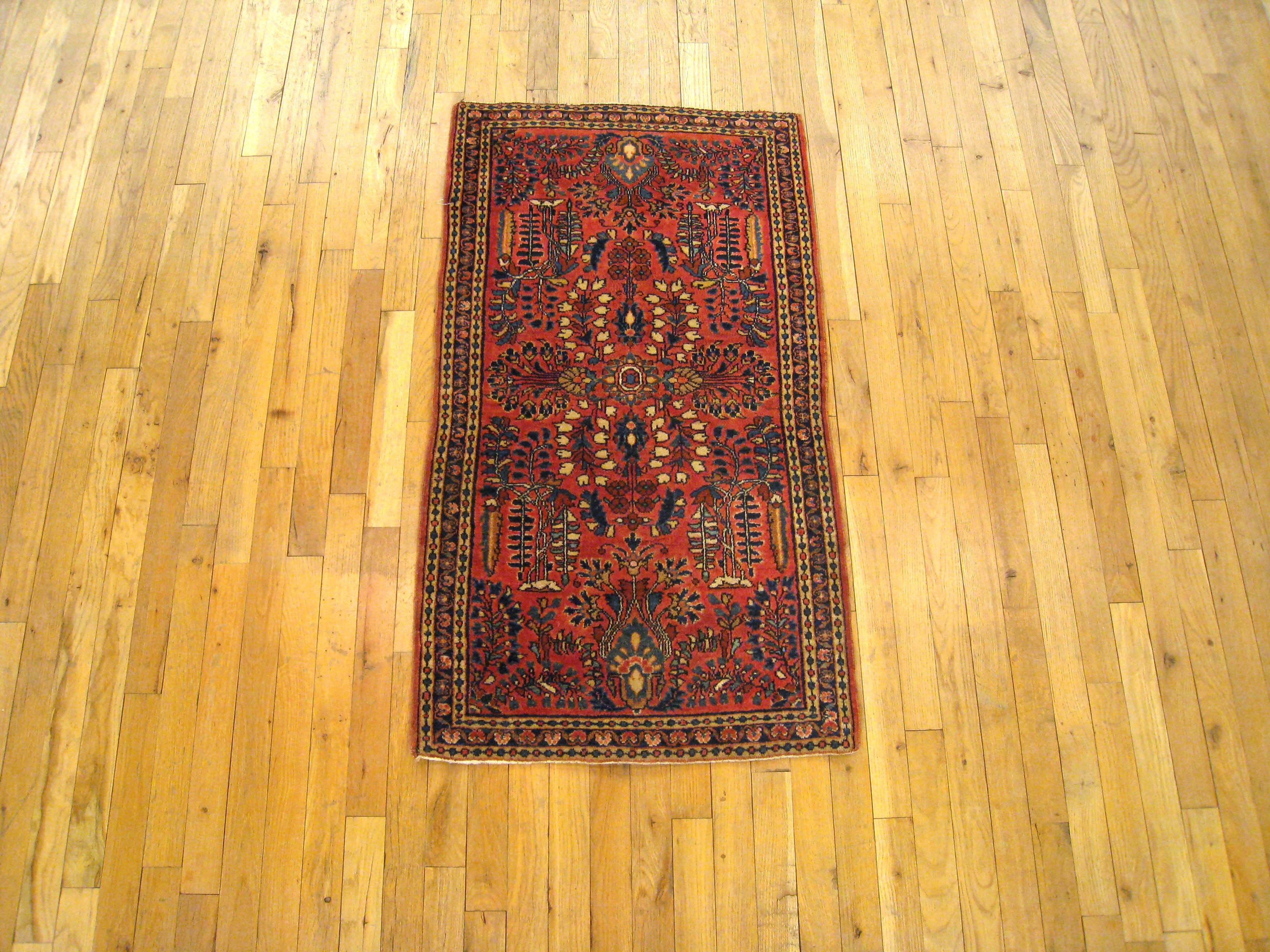 An antique Persian Sarouk oriental rug, size 4'0 x 2'2, circa 1920. This handsome hand-knotted Persian carpet features a symmetrical design in the red central field, consisting of neatly arranged floral elements and cypress trees. Enclosed within a