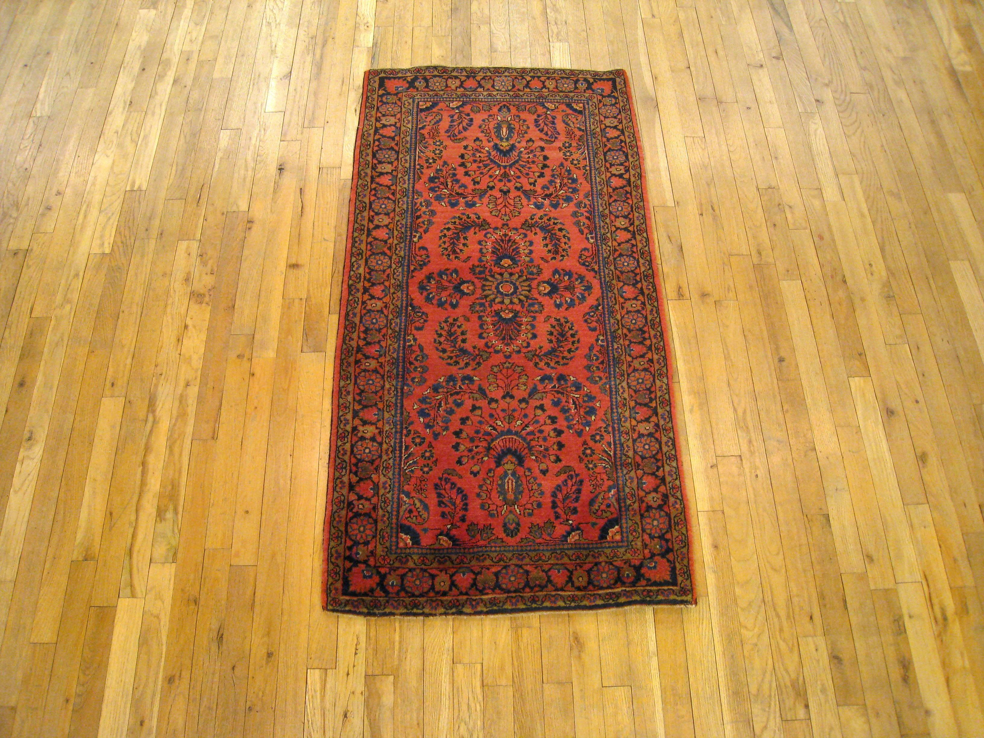 An antique Persian Sarouk oriental rug, size 5'0 x 2'6, circa 1920. This lovely hand-knotted Persian rug features a stylish floral design in the soft red central field, which is accentuated by the blue outer border with flower head design. Composed