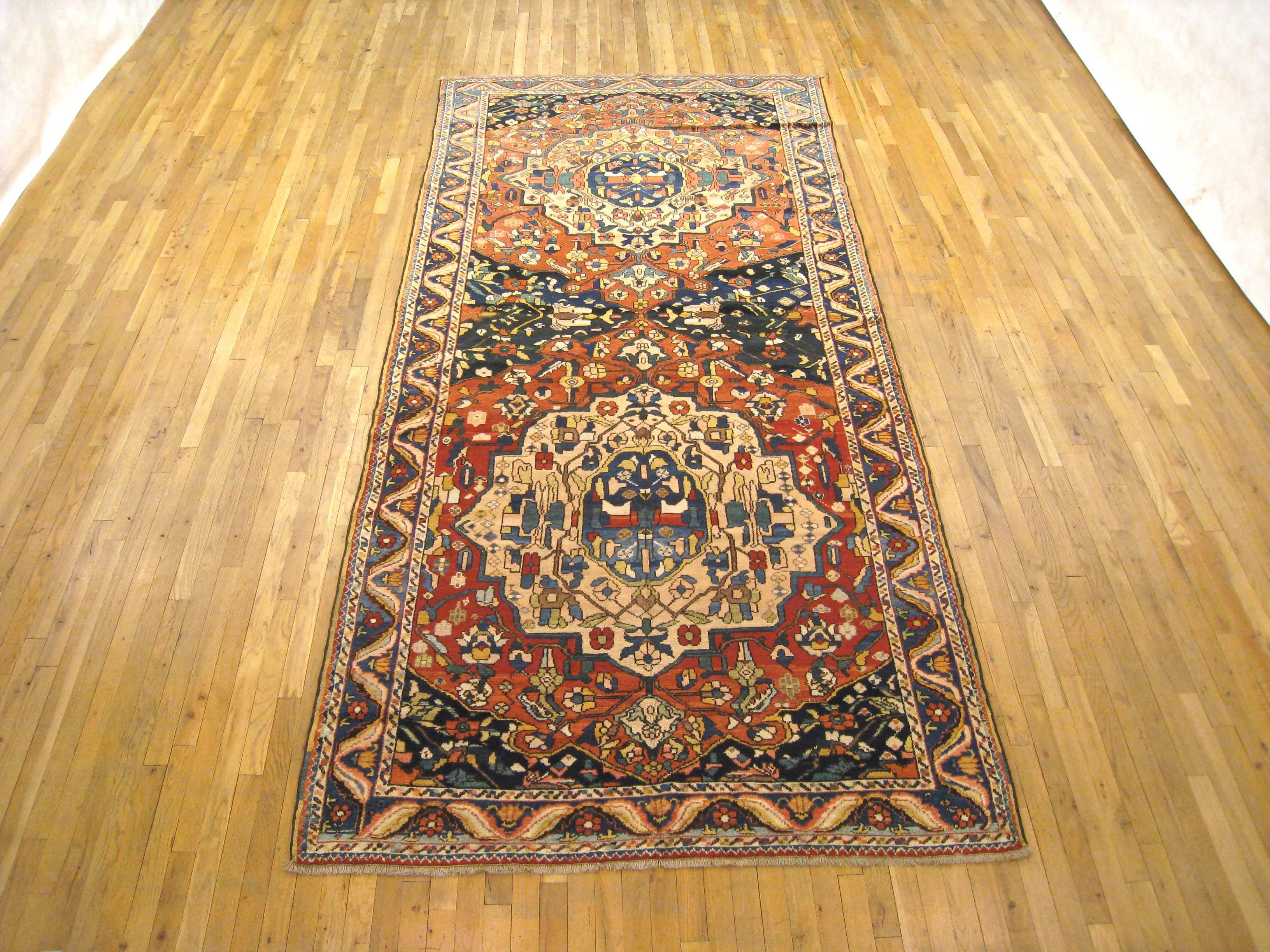 An antique N.W. Persian oriental rug, size 11'7 x 5'6, circa 1920-1930.  This handsome hand-knotted wool carpet features twin medallions in the central pane, with each of the two medallions seated within a soft red cartouche, and interconnected by a