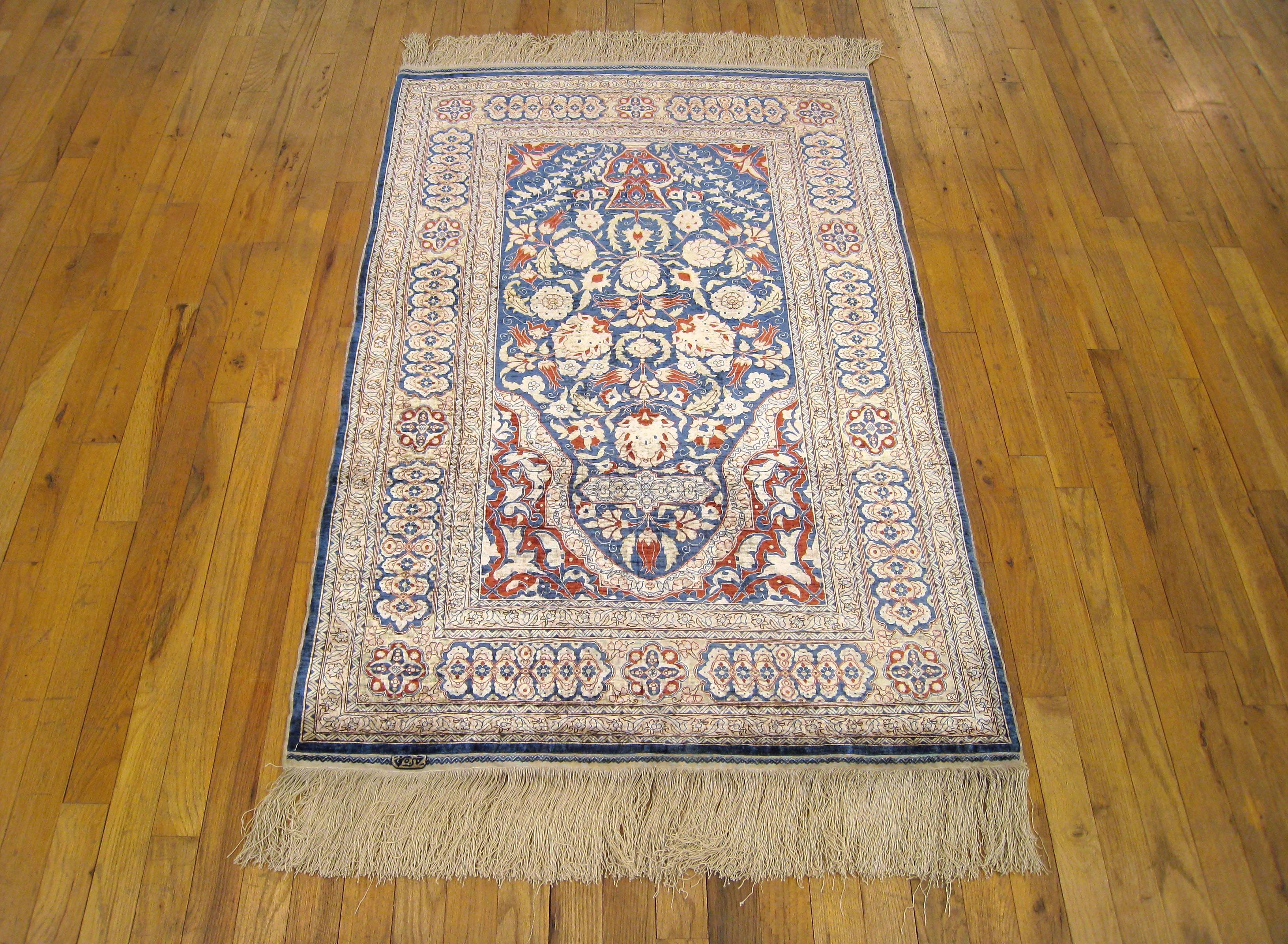 An antique Turkish silk Hereke oriental rug, size 4'6 H x 3'0 W, circa 1920. This fine hand-knotted carpet features a lustrous short silk pile with a vase design at one end of the blue center field, elegant flower heads at center and an arch at the