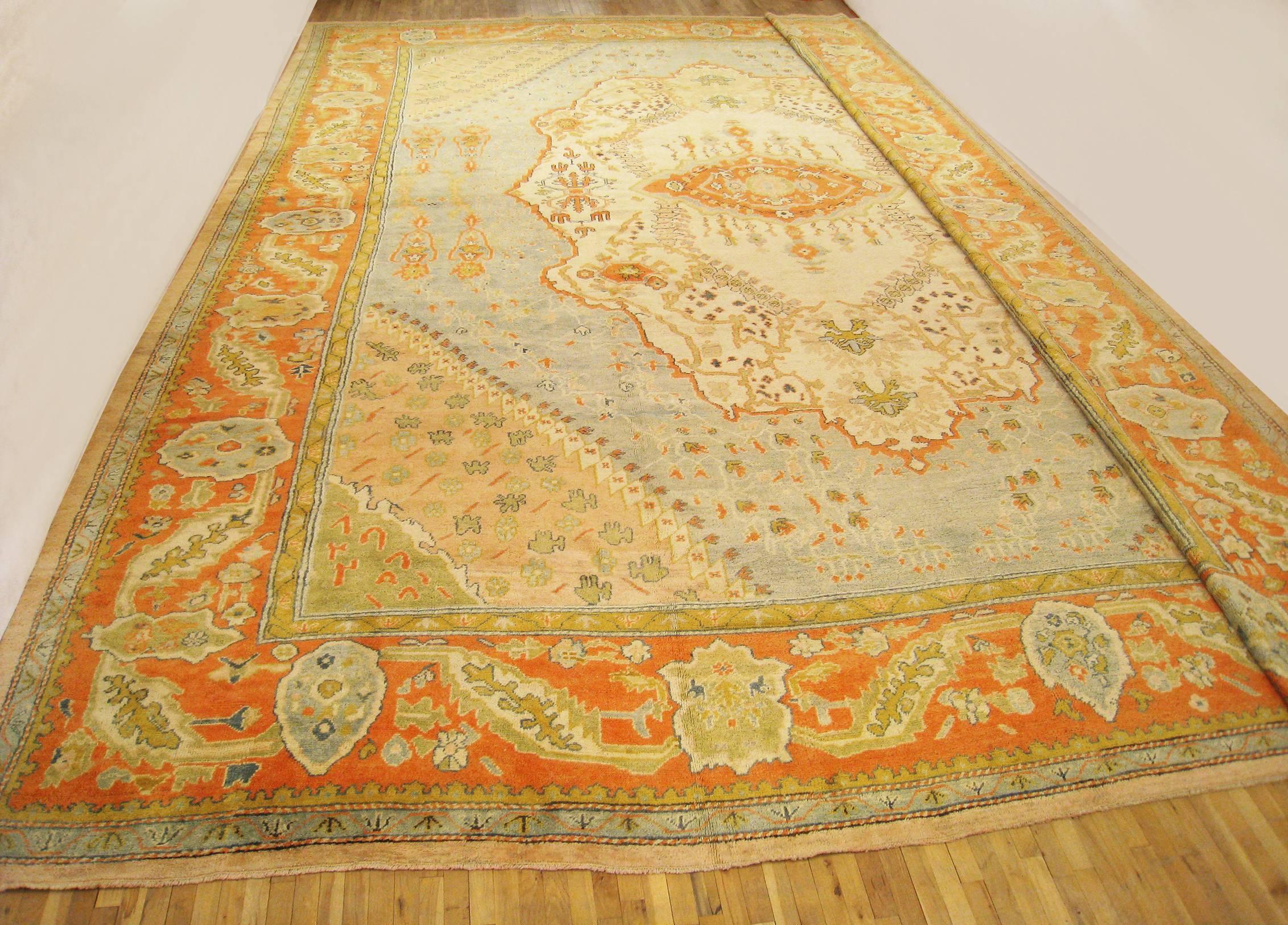 An antique Turkish Oushak oriental carpet, size 24'6 H x 19'6 W, circa 1900. This lovely hand-knotted wool carpet features a softly hued central medallion anchoring the pale blue primary field. The colors and design motifs of the central plane are