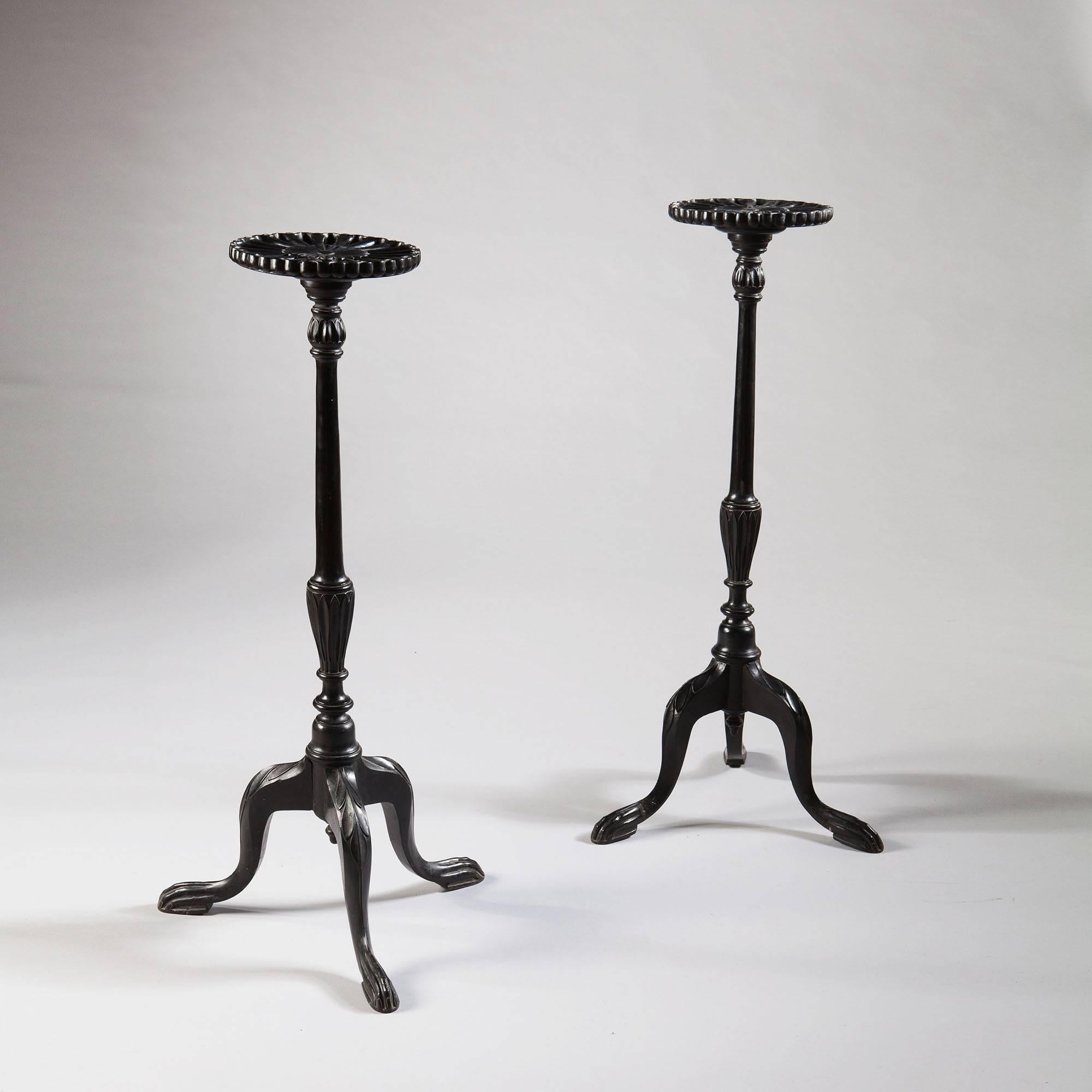 An elegant pair of tripod torcheres in ebonized wood with leaf carving to the base and tops carved in high relief as stylised flowers.