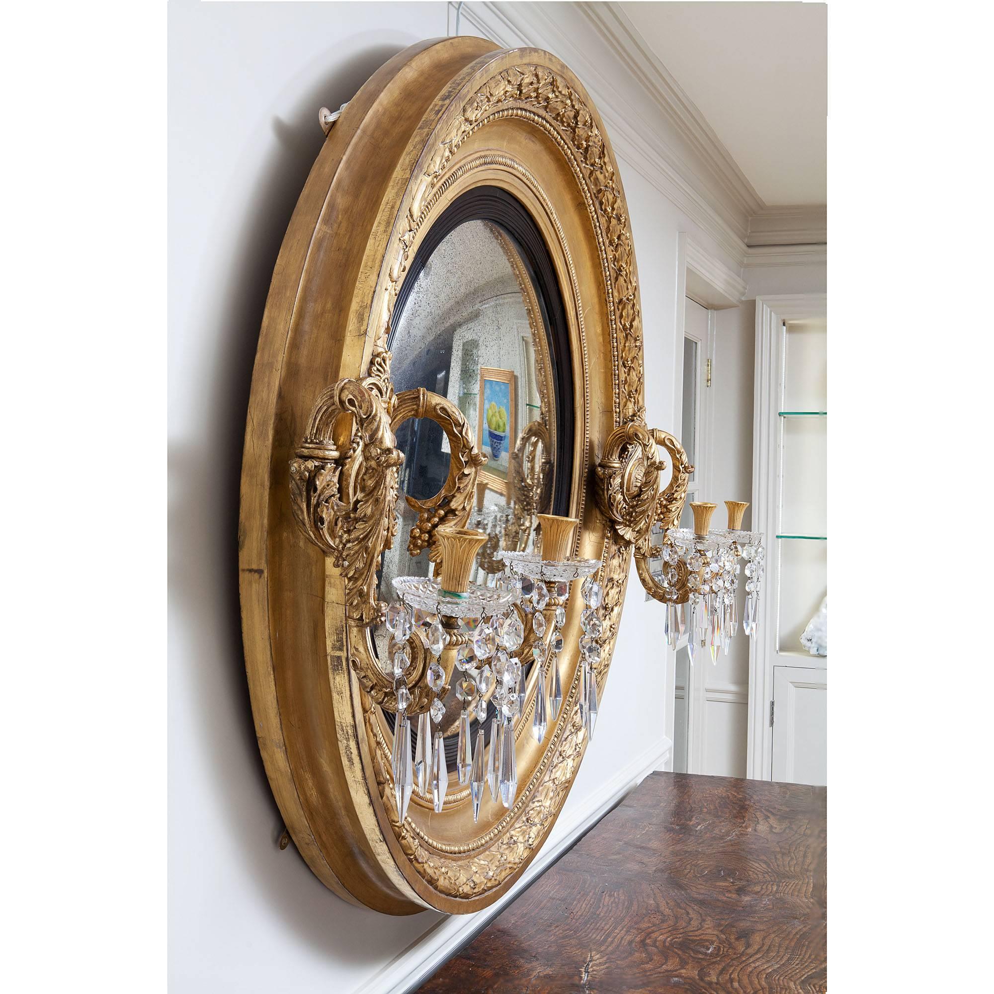 A truly fabulous, important, rare and grand proportioned Regency giltwood convex mirror. The substantial frame carved with overlapping laurel leaves and berries, supporting to boldly carved acanthus candelabra with original cut-glass drip pans and