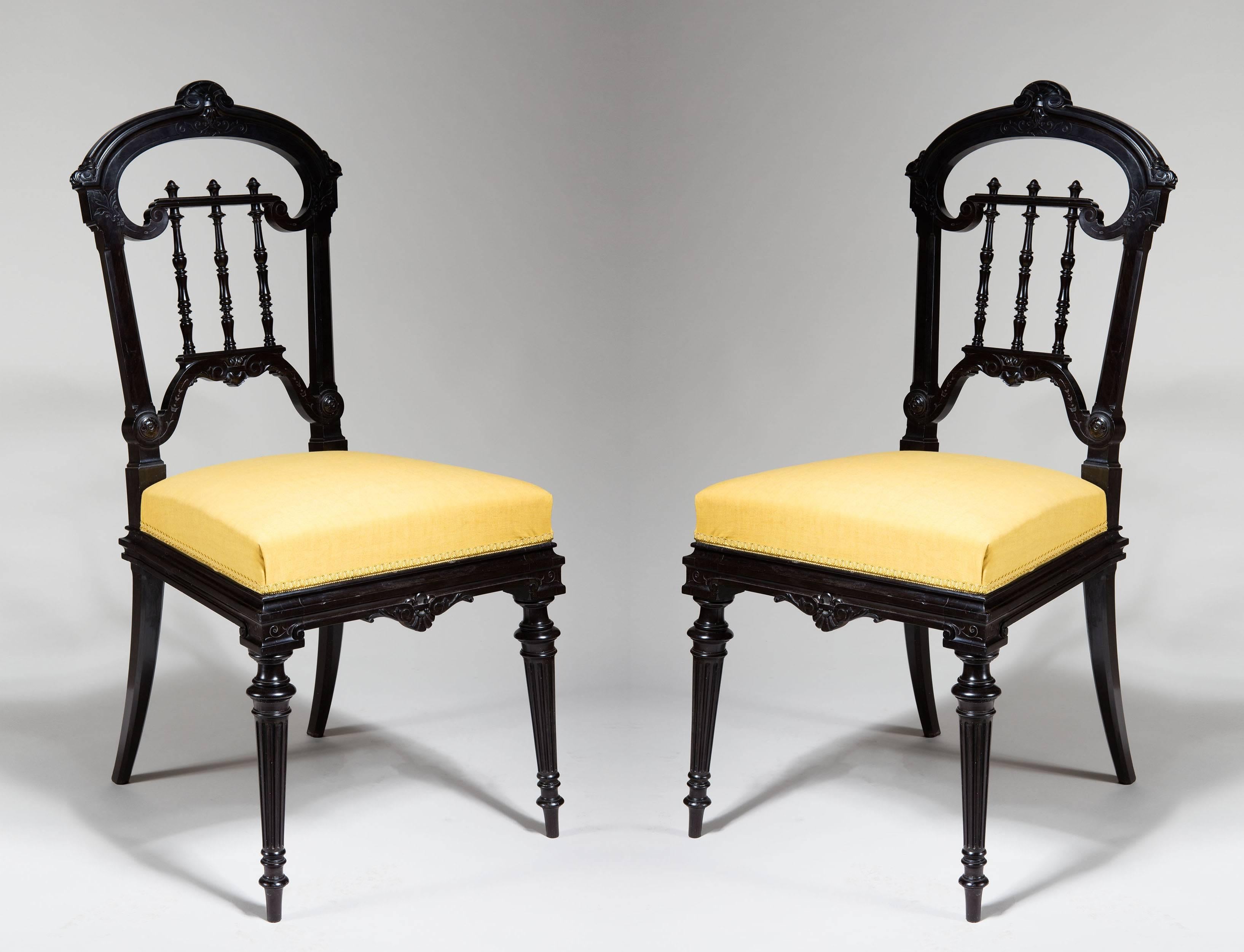 A pair of 19th century solid ebony chairs carved through in low relief with foliate decoration. The back splat fashioned as delicately turned spindles. Standing on turned legs at the front and sabre ones at the back.

The blocks underneath with