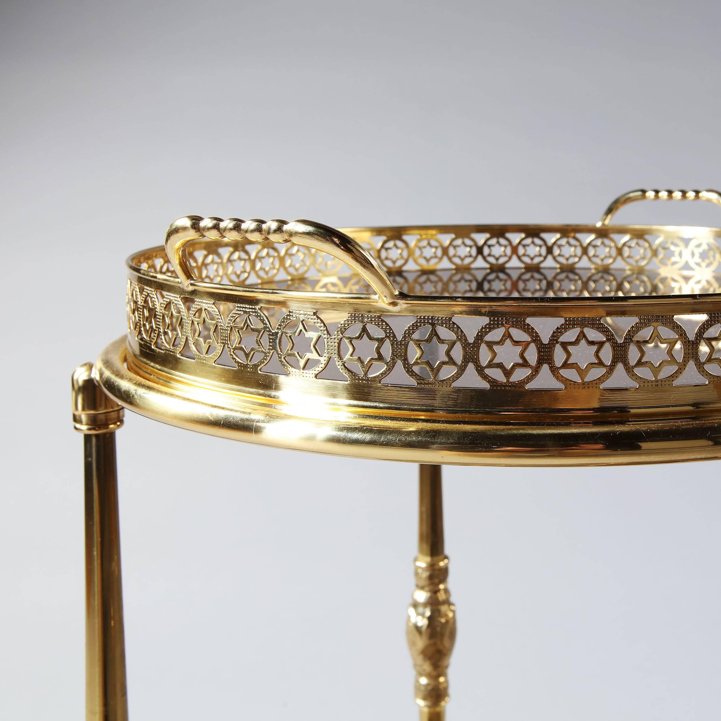 Super chic and very rare design of bar cart, with pierced stars around the borders of circular form, with two tiers, (the upper, a removable tray) with their original smoked glass, the lower level with a seven bottle holder and raised on four brass