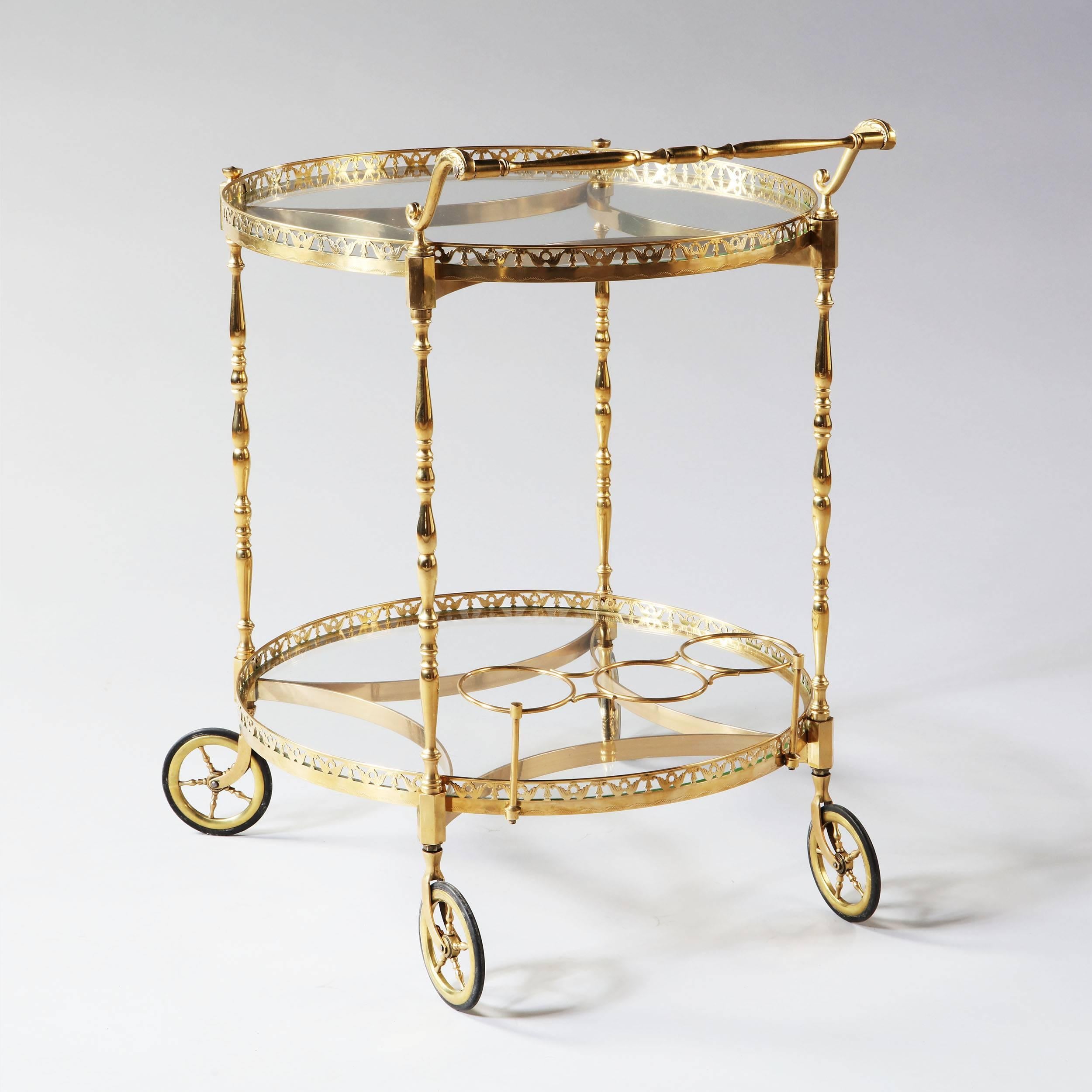 Fabulous and very fine circular polished brass bar cart with two levels, the borders of pierced brass supported on turned brass legs with concave stretchers, an ornate handle and raised on four brass wheels. 

Attributed to Maison